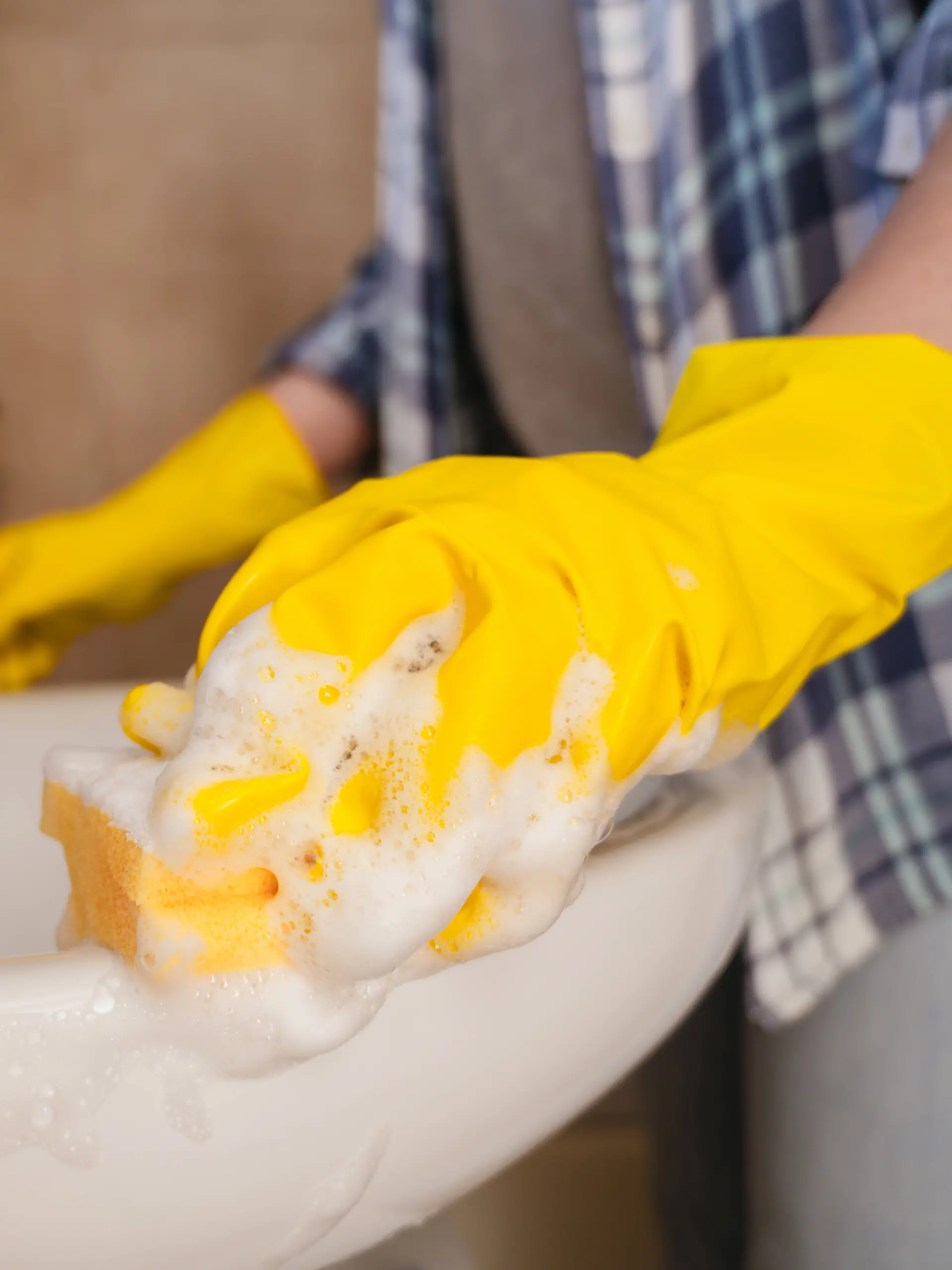 Frau reinigt Waschbecken im Badezimmer mit Gummihandschuh und Schwamm – Symbolbild