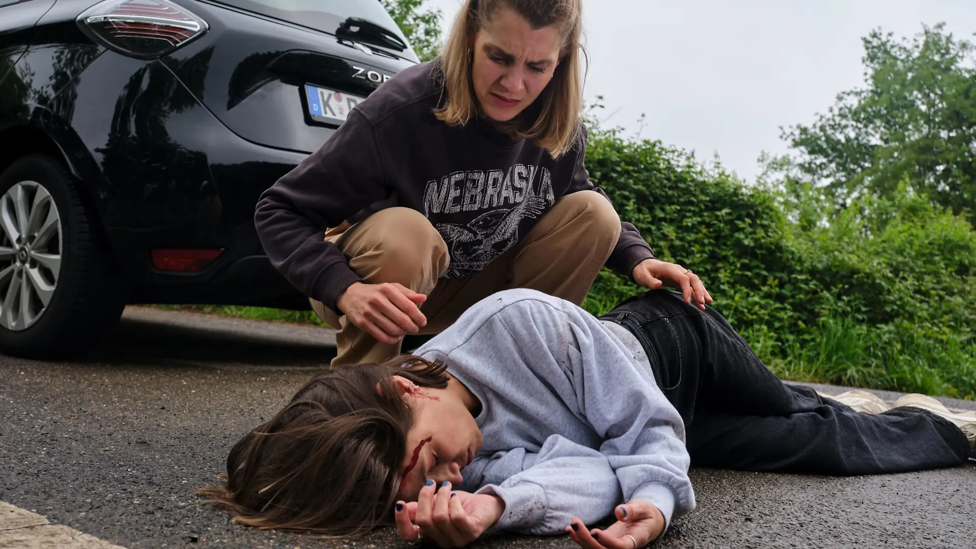 Stella (Bettine Langehein) erkennt entsetzt, dass es sich bei dem Unfallopfer um Charlotte (Anna Julia Antonucci, vorne) handelt.