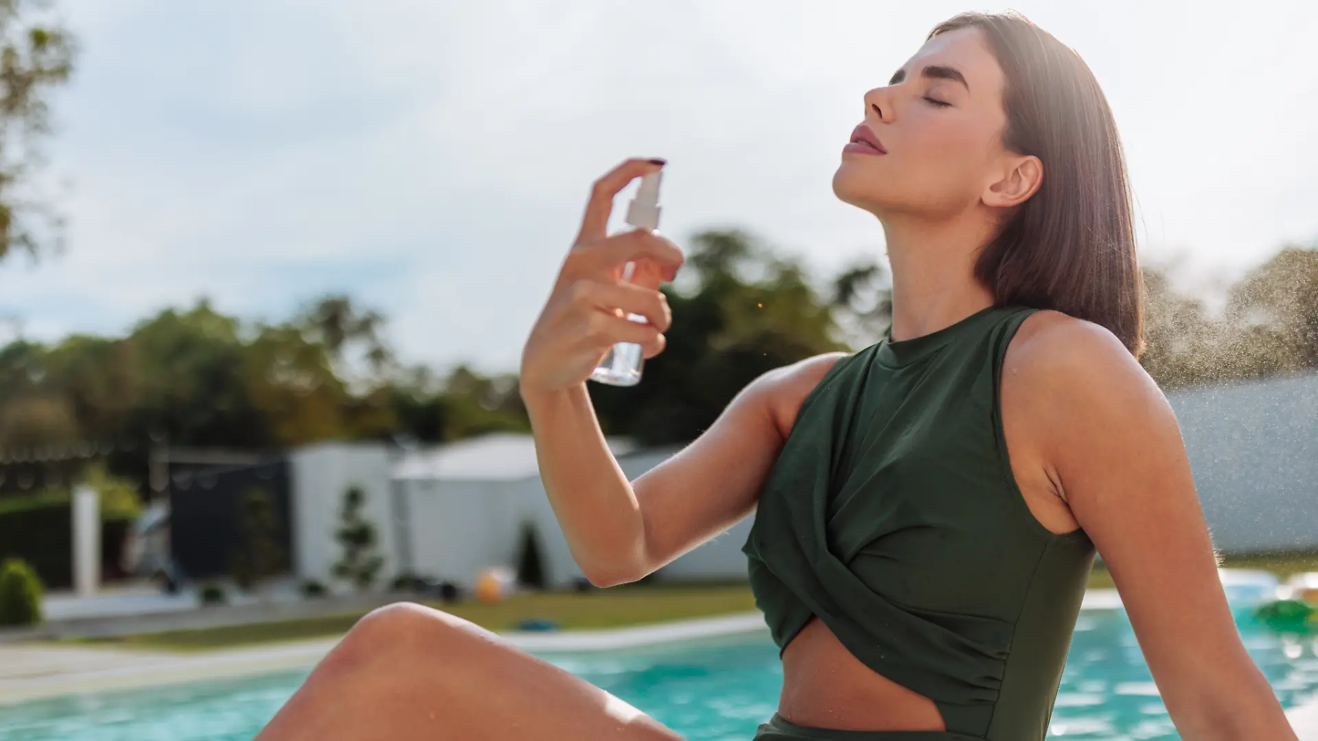 Frau sitzt am Pool und sprüht sich mit Bodyspray ein.