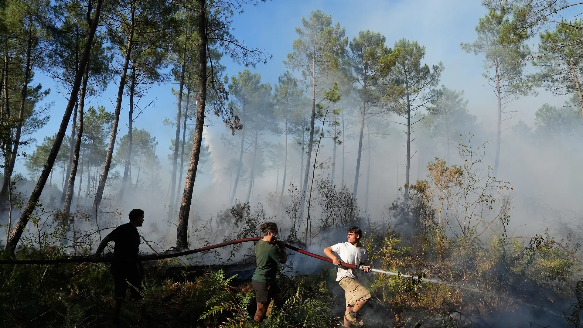 A group hold a firehose and try to suppress a fire near Lacanau, as wildfires rage outside Bordeaux, France, Monday, July 27, 2026. (AP Photo/Baz Ratner)