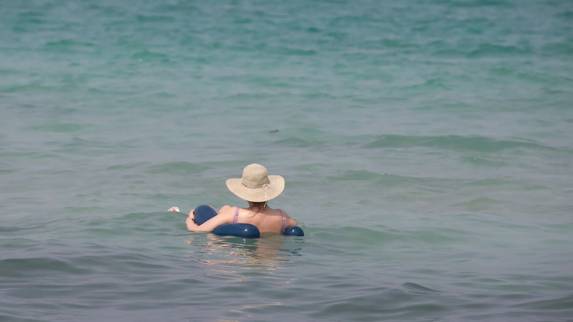 Eine Person entspannt sich am Strand von Can Picafort und schwimmt mit einem Sonnenhut auf dem Kopf im Wasser an der Nordküste von Mallorca. (zu dpa: «Rekord-Wassertemperatur vor Mallorca: 33,02 Grad») +++ dpa-Bildfunk +++