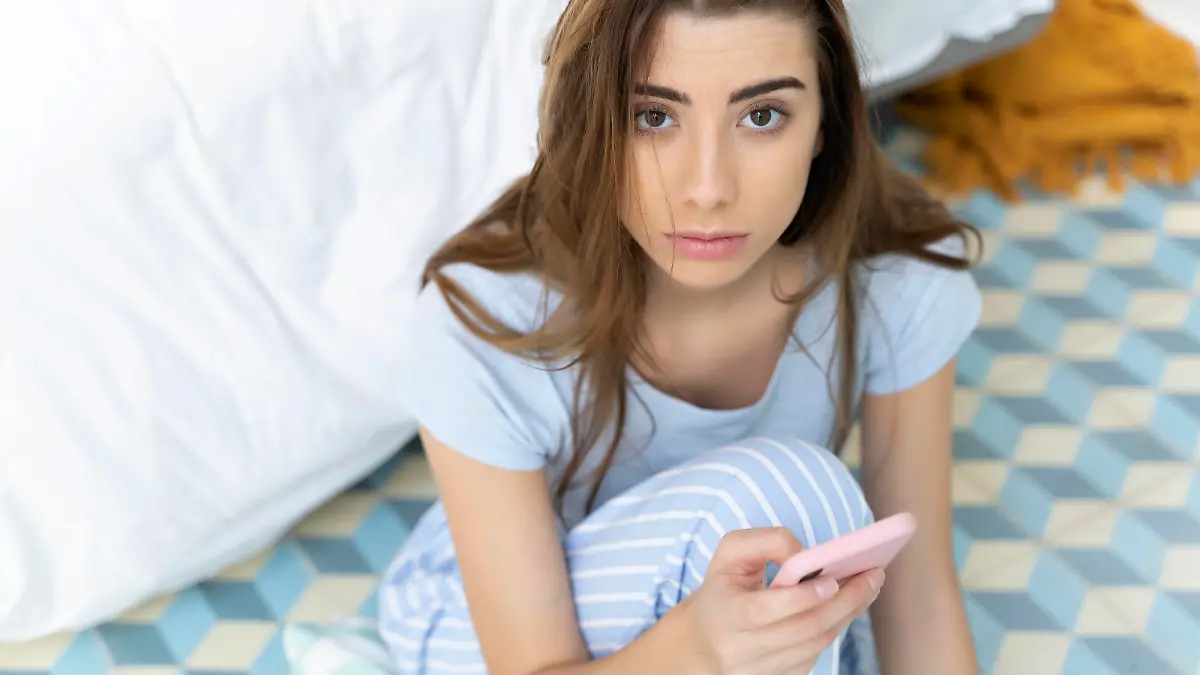 Portrait of young woman holding smartphone in bedroom model released Symbolfoto property released PUBLICATIONxINxGERxSUIxAUTxHUNxONLY ERRF02544