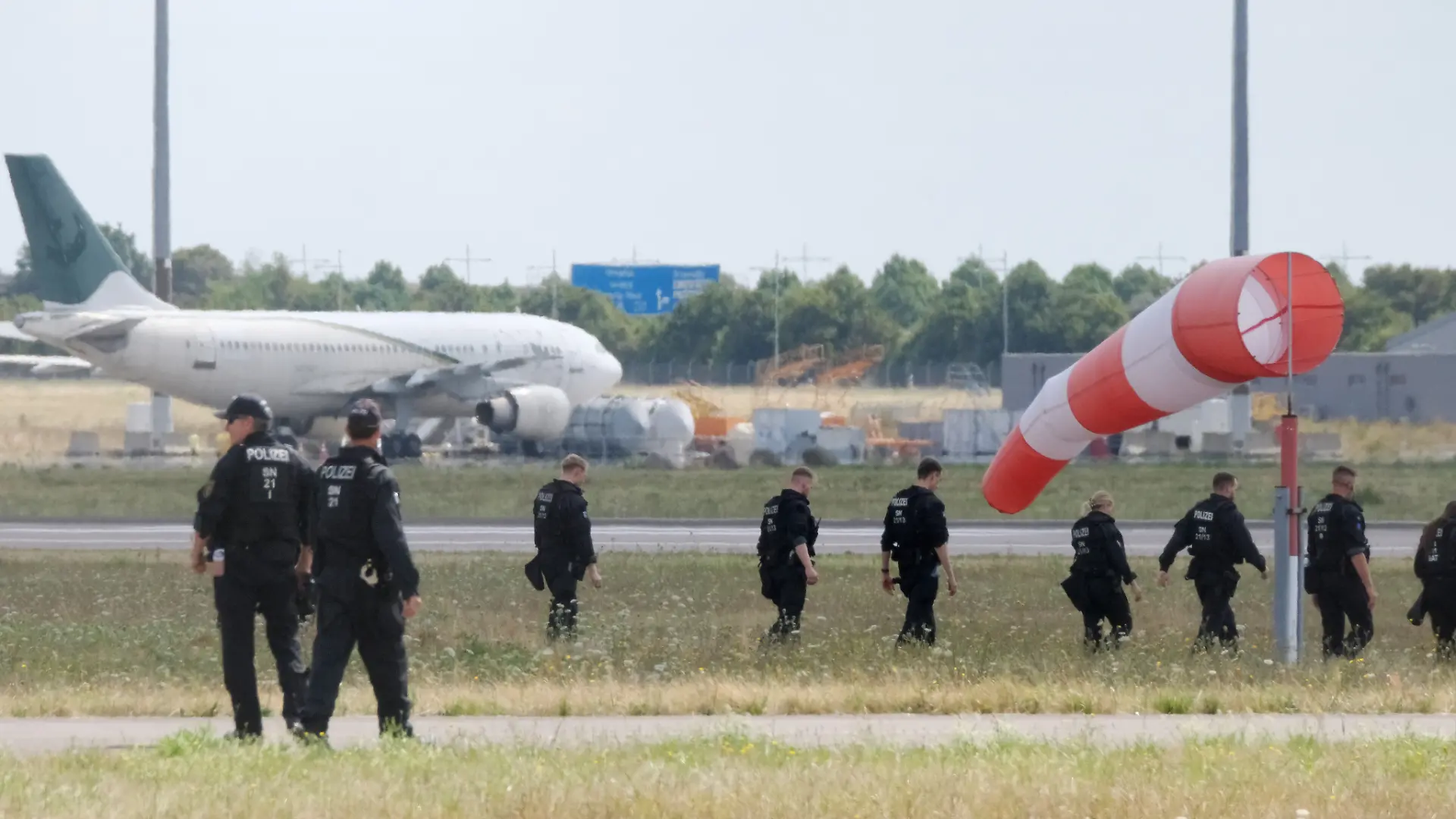 Polizisten gehen über eine Wiese auf dem Gelände des Flughafen-Leipzig. Die Ermittlungen nach der Entdeckung der Sprengstoff-Drohne dauern an. An der nördlichen Rollbahn sind zahlreiche Polizistinnen und Polizisten im Einsatz und suchen das Gelände zu Fuß ab.