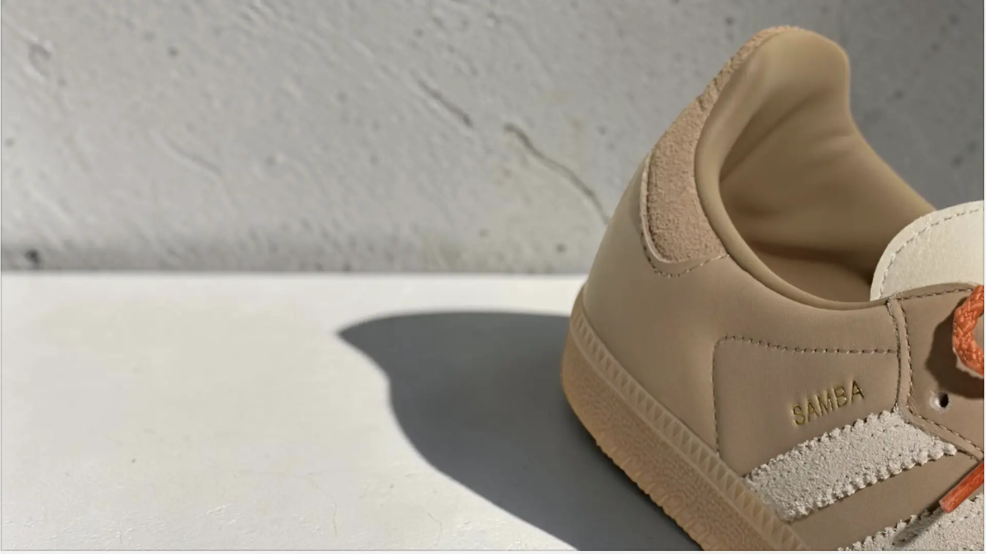 Ein Teil des Adidas Samba in Beige mit orangenem Schnürsenkel vor neutralem Hintergrund