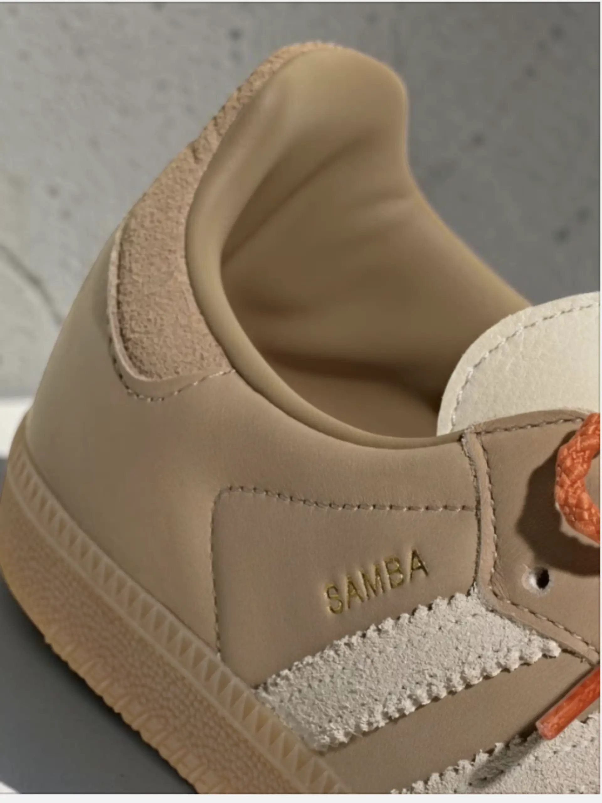 Ein Teil des Adidas Samba in Beige mit orangenem Schnürsenkel vor neutralem Hintergrund