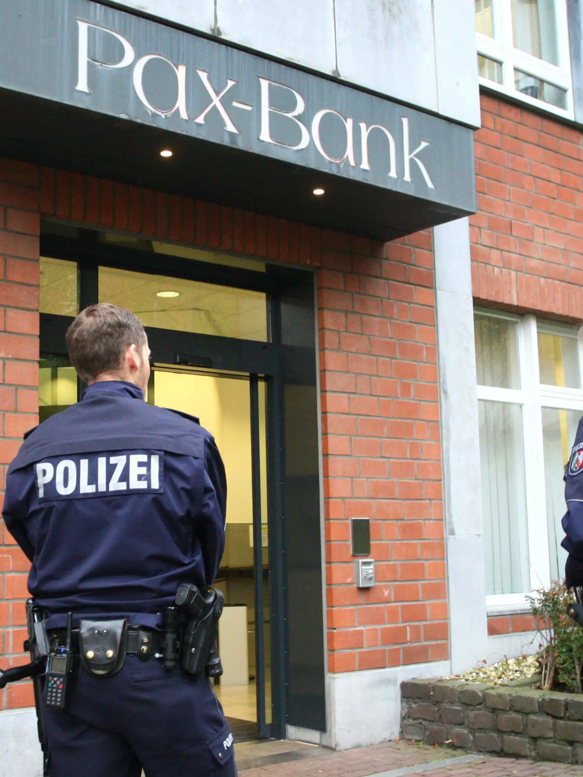 Einsatzkräfte stehen am 19.11.2014 in Aachen (Nordrhein-Westfalen) vor der Filiale der Pax-Bank. Sechs mit Perücken und Sonnenbrillen maskierte Bankräuber haben am Mittwoch in Aachen 16 Bankangestellte bedroht und sind dann mit ihrer Beute geflohen. Nach Polizeiangaben waren die dunkel gekleideten Räuber vor der offiziellen Öffnung in die Bank eingedrungen. Sie fingen nach und nach eintreffende Angestellte ab und bedrohten zuletzt 16 Beschäftigte. Einige davon seien gefesselt worden, sagte Polizeisprecher Werner Schneider. Mindestens eine Schusswaffe sei im Spiel gewesen. Foto: Ralf Roeger/dpa ++ +++ dpa-Bildfunk +++