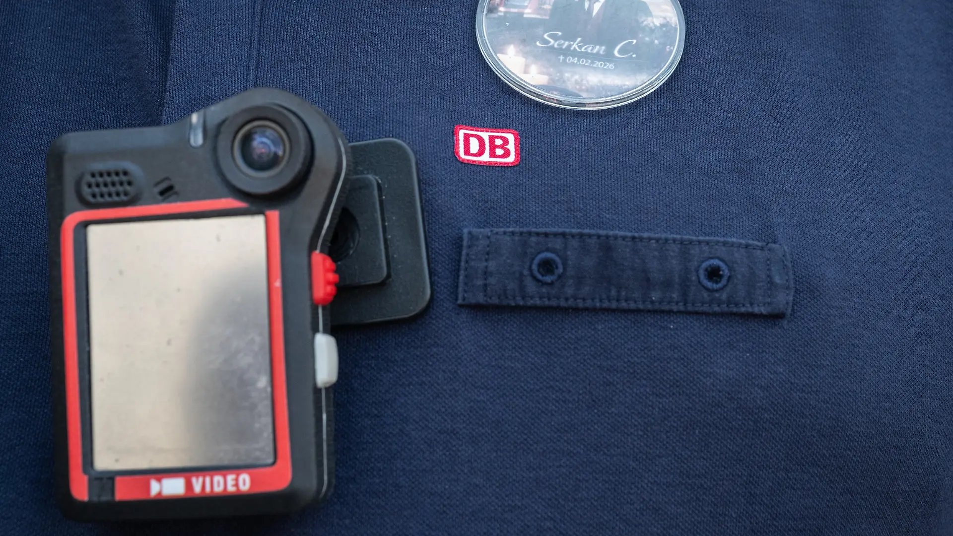 Ein Zugbegleiter trägt einen Anstecker mit dem Bild des verstorbenen Zugbegleiters und eine Bodycam. Fünf Monate nach dem brutalen Angriff auf einen Zugbegleiter in Rheinland-Pfalz ist der Angeklagte zu zehn Jahren Gefängnis verurteilt worden. +++ dpa-Bildfunk +++