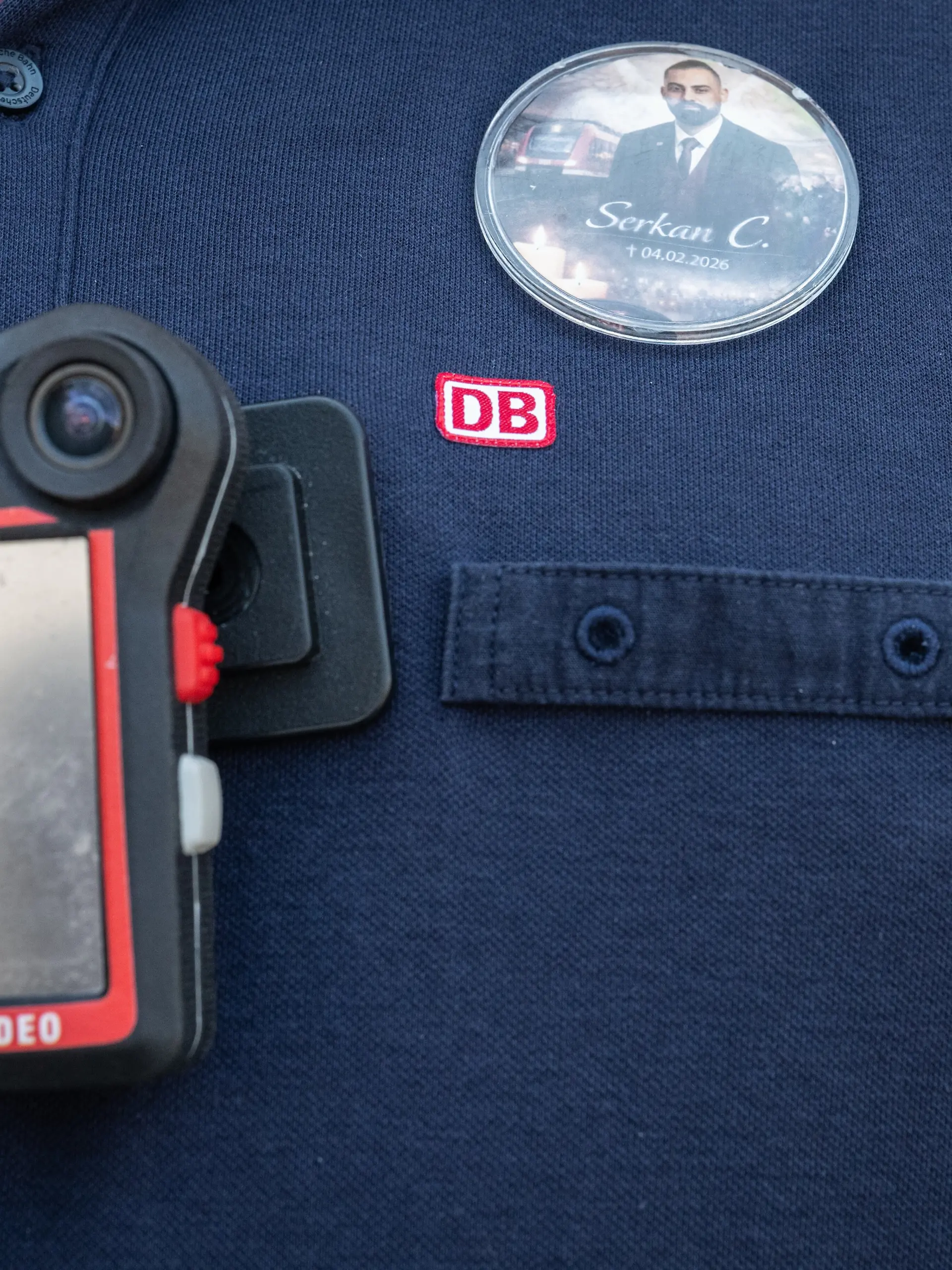Ein Zugbegleiter trägt einen Anstecker mit dem Bild des verstorbenen Zugbegleiters und eine Bodycam. Fünf Monate nach dem brutalen Angriff auf einen Zugbegleiter in Rheinland-Pfalz ist der Angeklagte zu zehn Jahren Gefängnis verurteilt worden. +++ dpa-Bildfunk +++