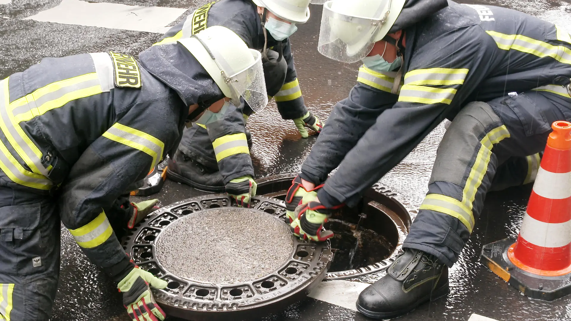 Nach einem heftigen Gewitterregen setzen Feuerwehrleute Kanaldeckel wieder ein, die durch den Druck in der Kanalisation herausgehoben wurden.