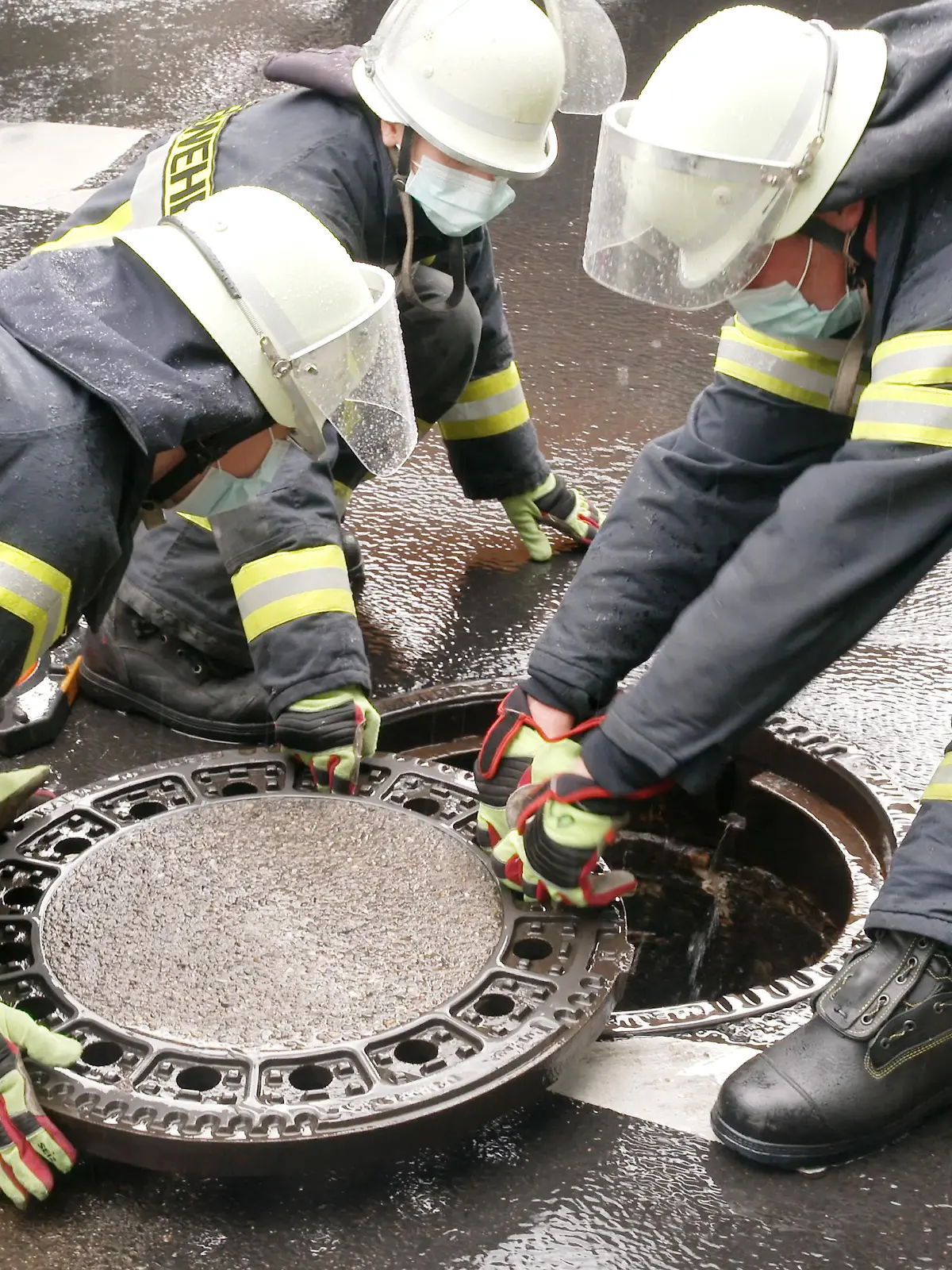 Nach einem heftigen Gewitterregen setzen Feuerwehrleute Kanaldeckel wieder ein, die durch den Druck in der Kanalisation herausgehoben wurden.