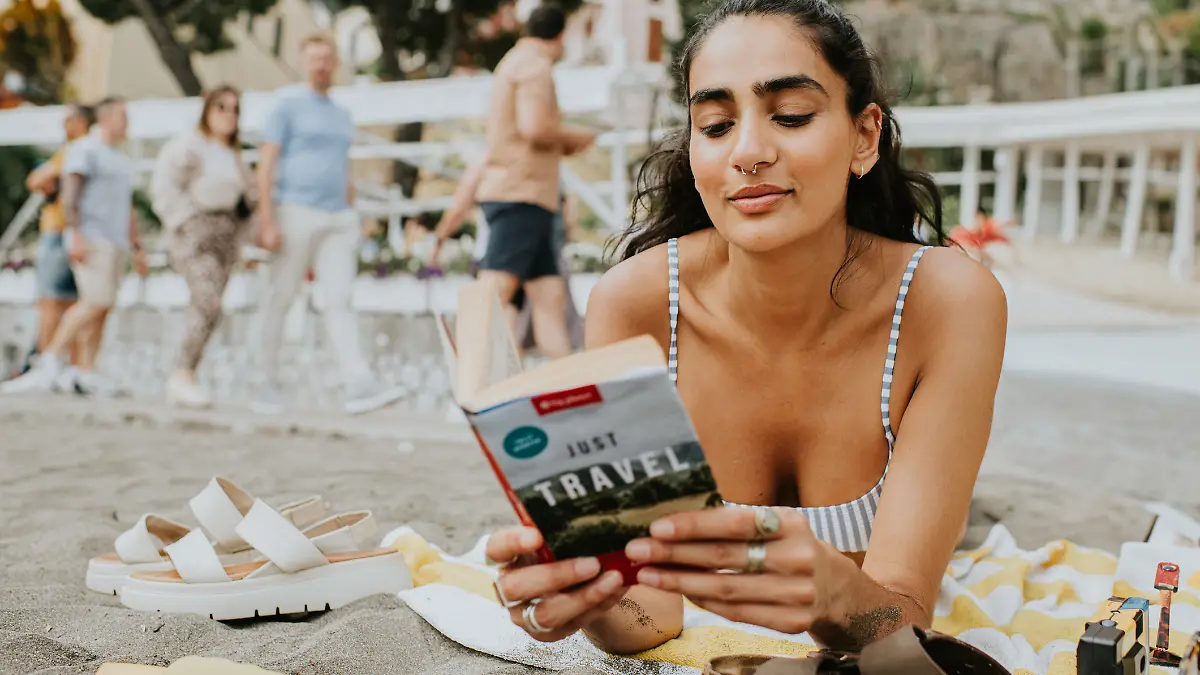 Frau liegt alleine am Strand und liest ein Buch