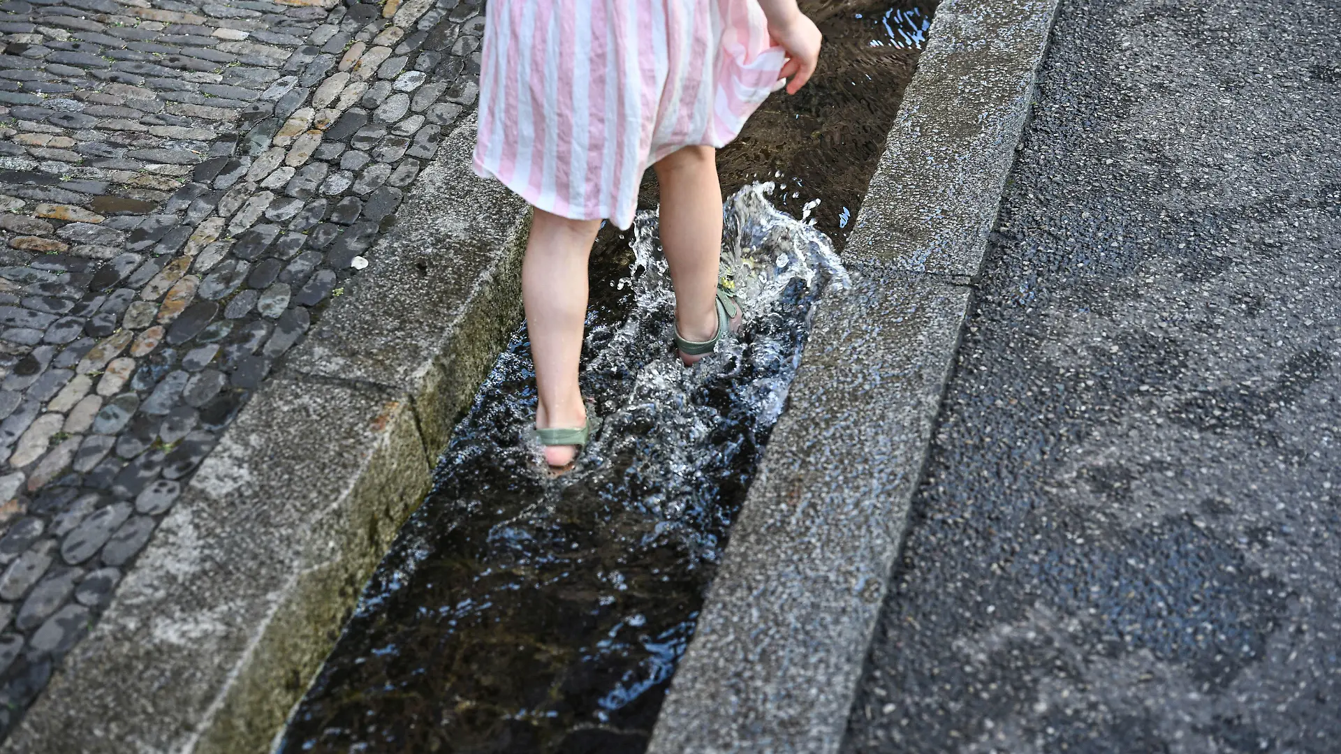 Sommer, Hitze, Abkuehlung a la Freiburg. Ein Maedchen sucht Erfrischung in einem der zahlreichen kleinen Kanaele, den sogenannten "Baechle", die die Freiburgerv Innenstadt schmuecken. Foto: Winfried Rothermel