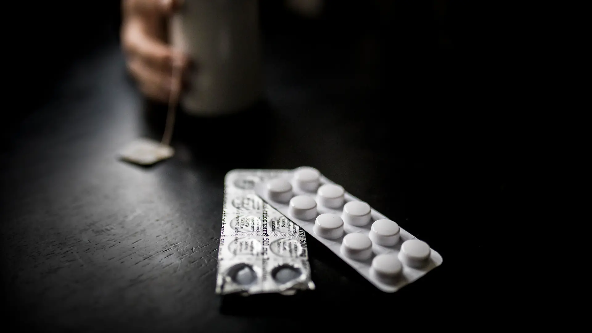Tabletten (Paracetamol) zeichnen sich vor einer Tasse Tee ab.