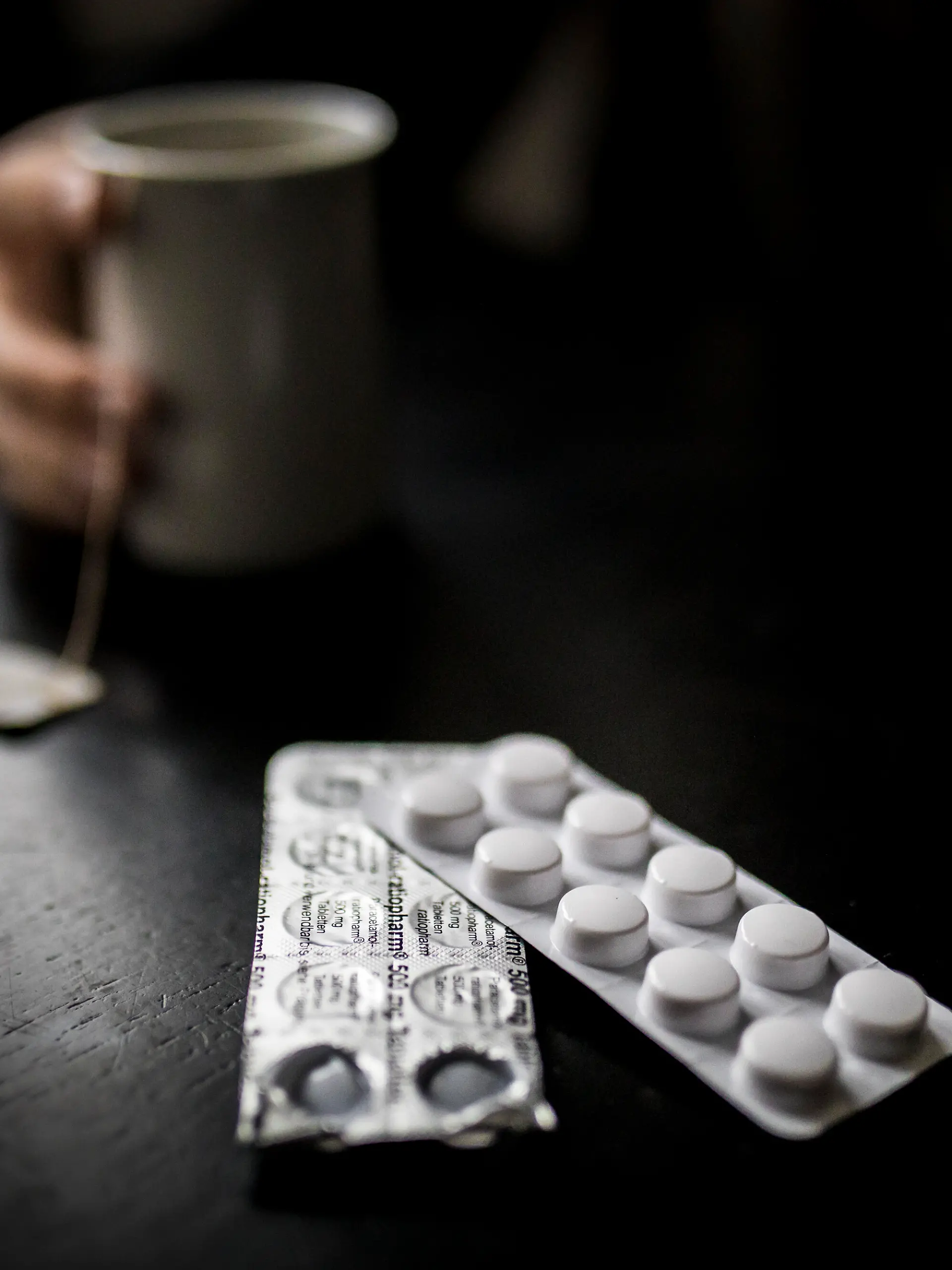 Tabletten (Paracetamol) zeichnen sich vor einer Tasse Tee ab.