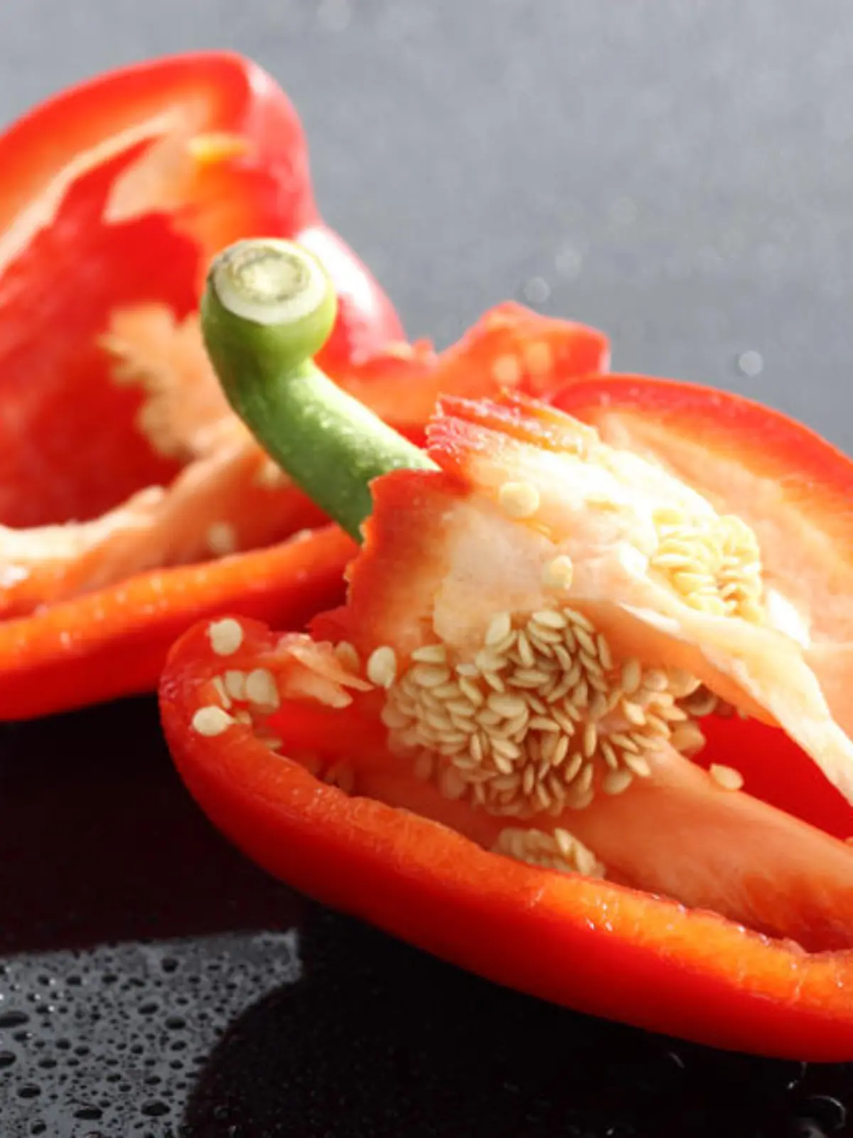 Zwei halbe rote Paprikaschoten auf schwarzem Acryl mit Wassertropfen.Nahaufnahme.Die Gattung Paprika (Capsicum), umgangssprachlich auch als Chili, Peperoni oder Pfefferoni bezeichnet (siehe Etymologie), gehÜrt zur Familie der NachtschattengewŠchse (Solanaceae). Es gibt viele verwandte Kulturpflanzenarten, wie z. B. Kartoffeln (Solanum tuberosum), Tomaten (Solanum lycopersicum), Auberginen (Solanum melongena) und auch alle Tabakarten (Nicotiana). Es wird sowohl die Pflanze als auch die Frucht als Paprika bezeichnet, vor allem fŸr die Frucht gibt es noch weitere Namen, die Unterschiede in SchŠrfe, GrÜße und auch Farbe kennzeichnen. Die am weitesten verbreitete Art, zu der auch fast alle in Europa erhŠltlichen Paprika, Peperoni und Chilis gehÜren, ist Capsicum annuum. Die meisten Paprika enthalten den fŸr die SchŠrfe verantwortlichen Stoff Capsaicin, erst in den 1950er Jahren wurden mit den GemŸsepaprika milde Sorten gezŸchtet, die fast keine Scharfstoffe mehr enthalten.Der Paprikageschmack ist zum grÜßten Teil auf ein Štherisches …l zurŸckzufŸhren. Der Anteil an langkettigen Kohlenwasserstoffen, FettsŠuren und deren Methylestern betrŠgt weniger als ein Prozent. FŸr den Paprikageruch bedeutsam sind Alkylmethoxypyrazine, etwa das ãerdigÒ riechende 3-Isobutyl-2-methoxypyrazin. Reife Paprika enthalten auch bis zu 6 ucker.Paprika enthŠlt relativ viel Vitamin C (0,1Ð0,4 Gewichtsprozent). So gelang es erstmals dem ungarischen Chemiker Albert Szent-GyÜrgyi, Vitamin C aus Paprika in genŸgender Menge zu isolieren. Er erhielt dafŸr 1937 den Nobelpreis fŸr Medizin. Paprikaschoten enthalten außerdem viele Flavonoide und Carotine [2]100 g rohe Paprika enthalten 19 kcal, 1,1 g Protein, 3 g Kohlenhydrate und 0,29 g Fett. Weitere wichtige Inhaltsstoffe sind etwa: 290 mg Kalium, 20 mg Magnesium, 15 mg Calcium pro 100 g Paprika.