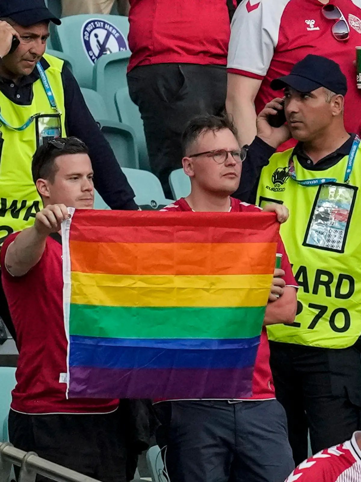 03.07.2021, Aserbaidschan, Baku: Fußball: EM, Tschechien - Dänemark, Finalrunde, Viertelfinale im Baku Olympic Stadium. Ordner stehen neben zwei Dänemark Fans die eine Regenbogen-Fahne hochhalten. Foto: Darko Vojinovic/Pool AP/dpa +++ dpa-Bildfunk +++
