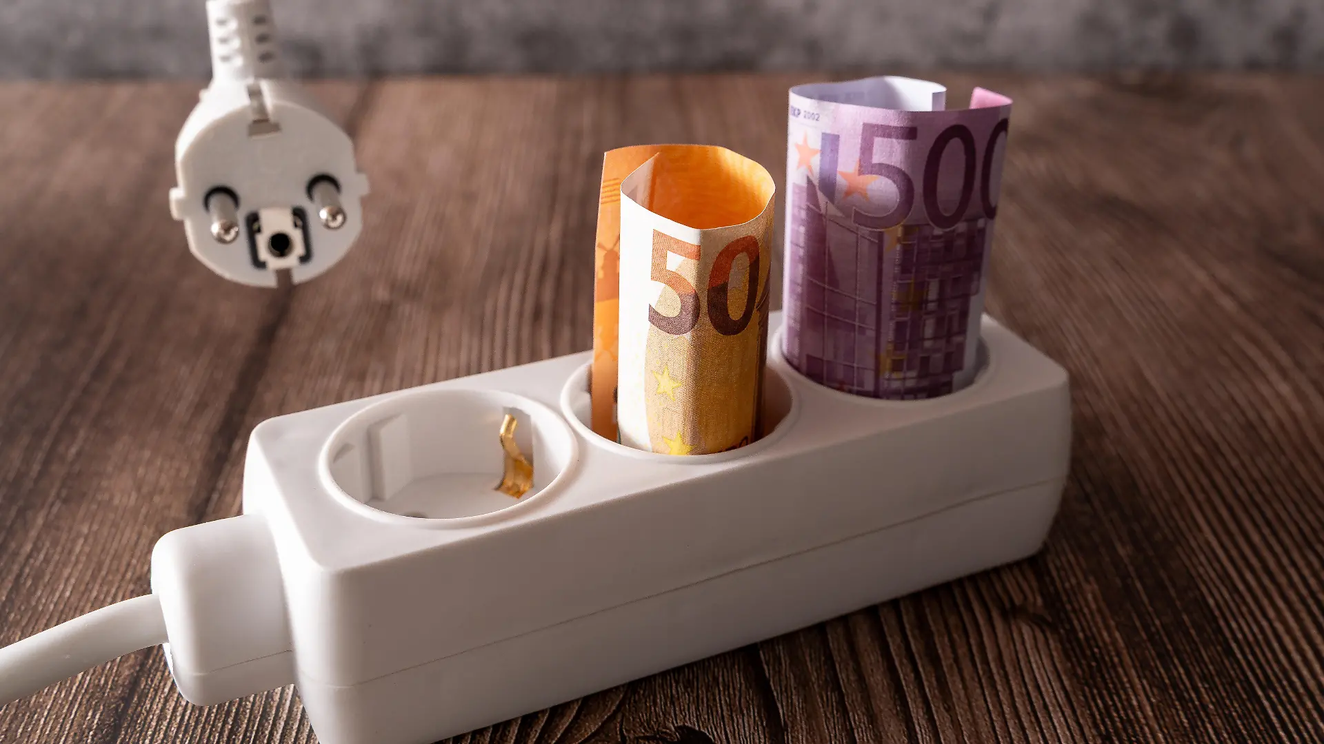 Gerollte Euro-Banknoten stecken in einer Steckdosenleiste