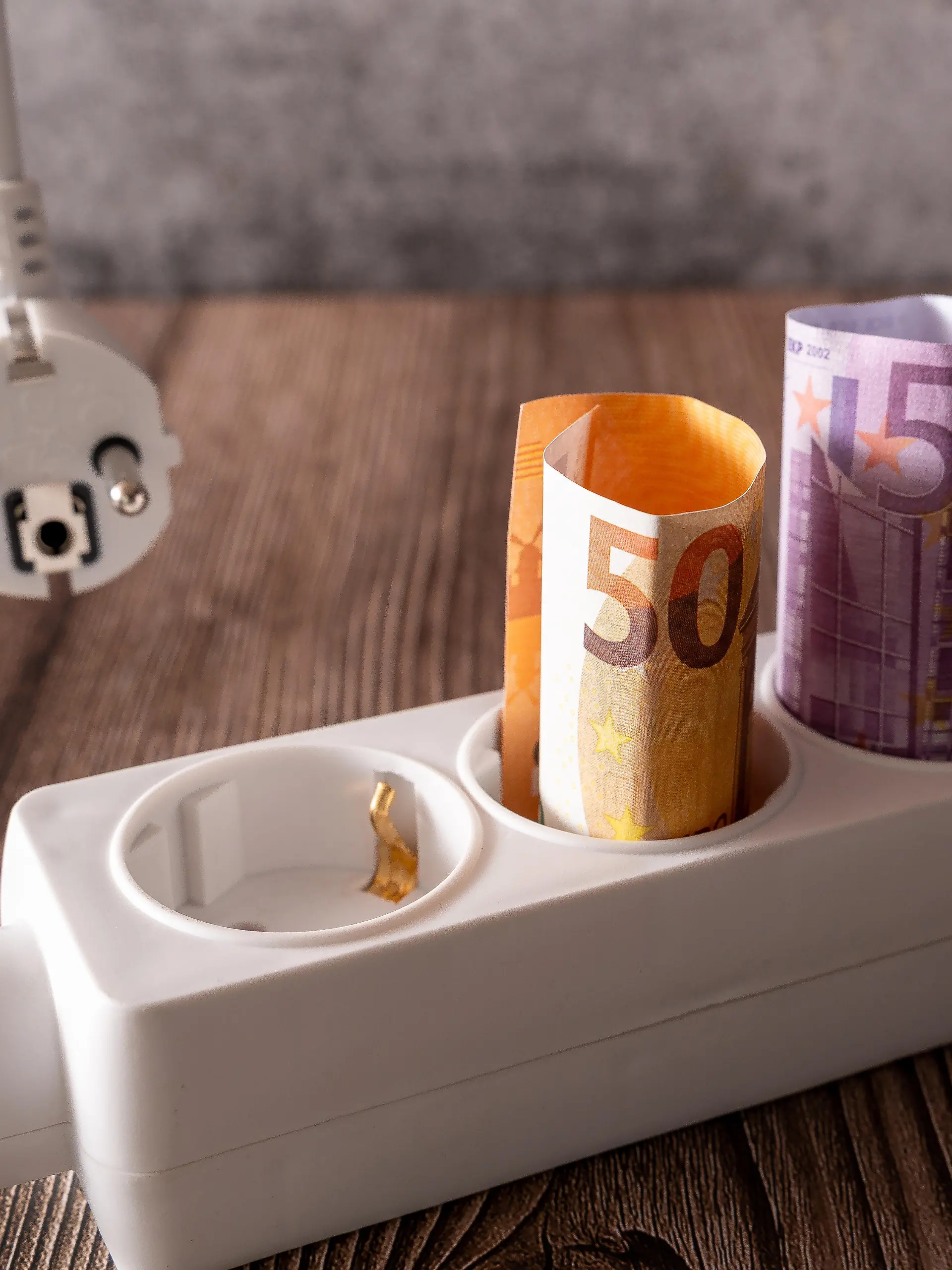 Gerollte Euro-Banknoten stecken in einer Steckdosenleiste