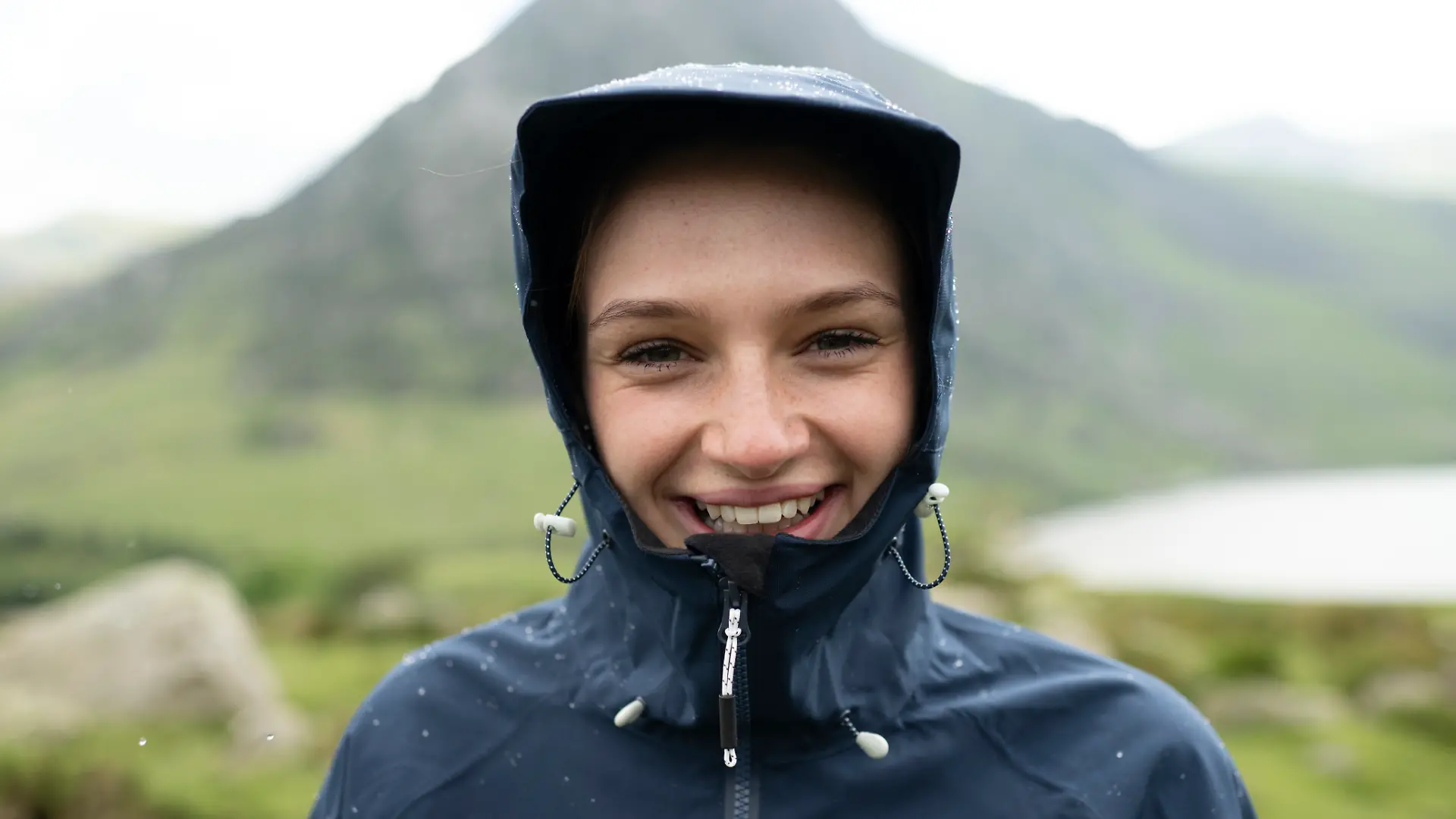 Nahaufnahme einer Frau in Regenjacke, im Hintergrund Berge.