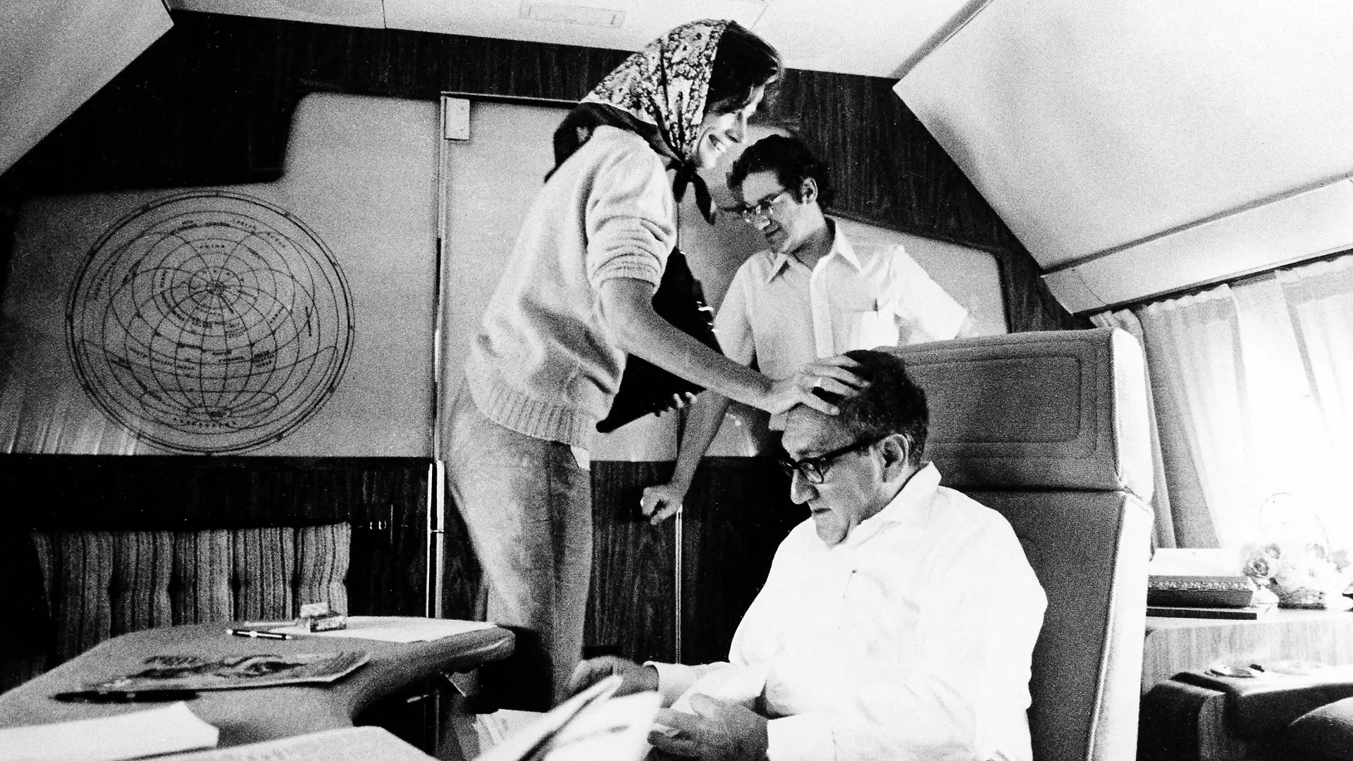 Nancy Kissinger playfully greets her husband, Secretary of State Henry Kissinger, as he studies newspapers on the shuttle flight between Israel and Egypt, on September 4, 1975. Standing at rear is National Security staff member Peter Rodman. (AP Photo)