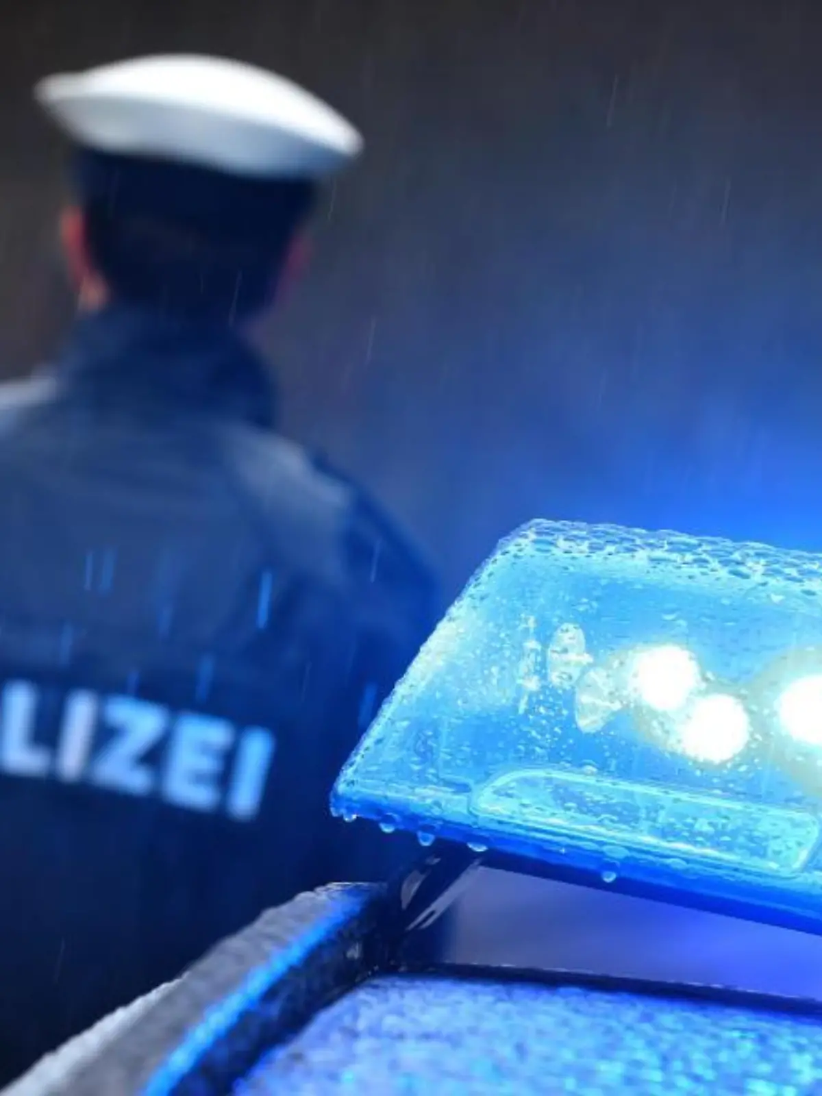 Ein Polizist steht im Regen vor einem Streifenwagen