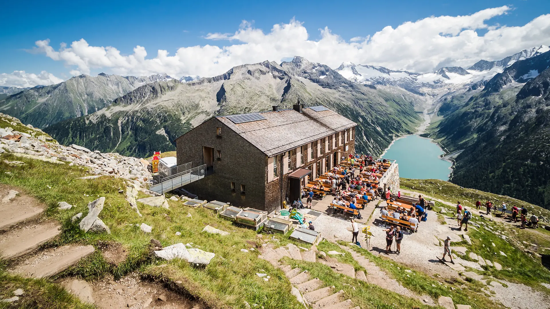 Tourists have rest at Olpererhutte mountain hut in Zillertal in Austrian Alps with beautiful scenery view above lake