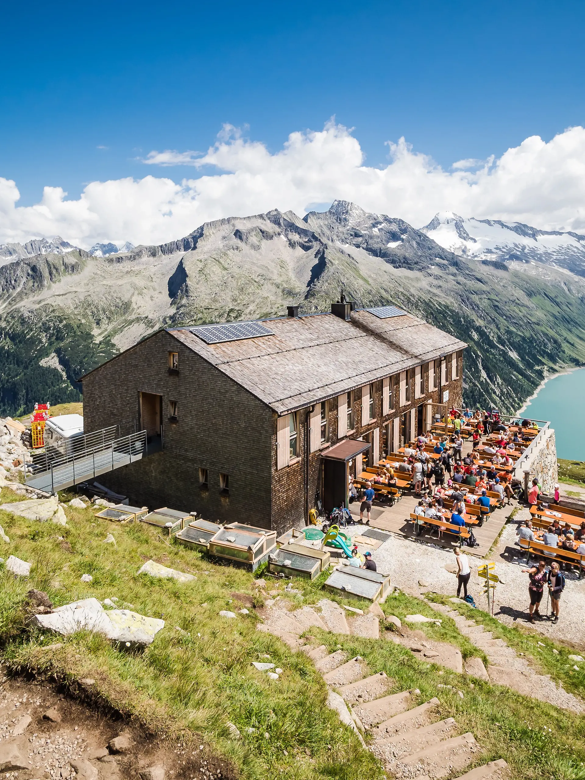 Tourists have rest at Olpererhutte mountain hut in Zillertal in Austrian Alps with beautiful scenery view above lake