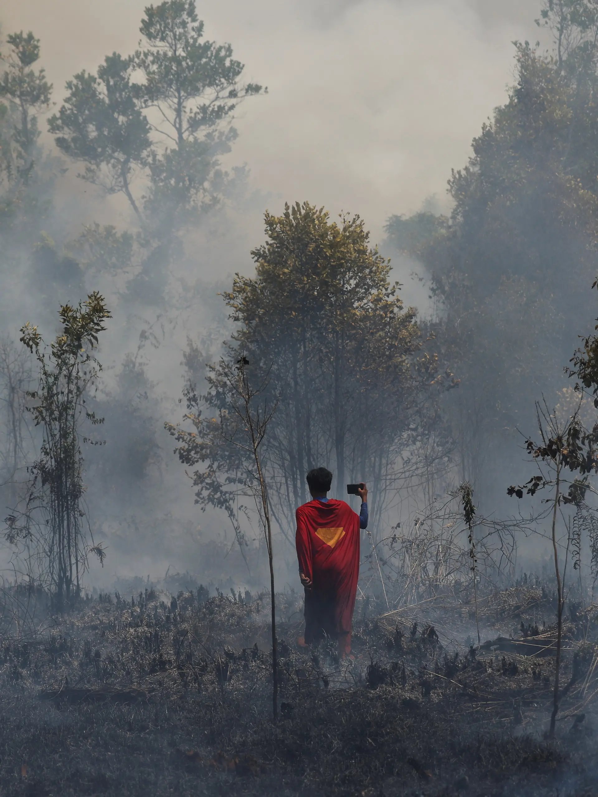 Rudiyansah, 16, wears a Superman costume inspects a fire at a wildfire-affected area in Palangka Raya, Central Kalimantan province, Indonesia, August 14, 2026. REUTERS/Ajeng Dinar Ulfiana