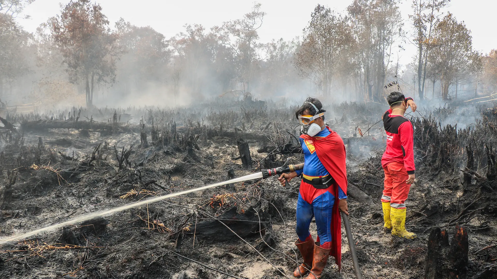 In this photo taken on August 17, 2026 Indonesian student Rudiansyah (L) dressed in a Superman costume helps to extinguish a forest and land fire at Petuk Katimpun in Palangkaraya, Central Kalimantan. (Photo by REINA / AFP)