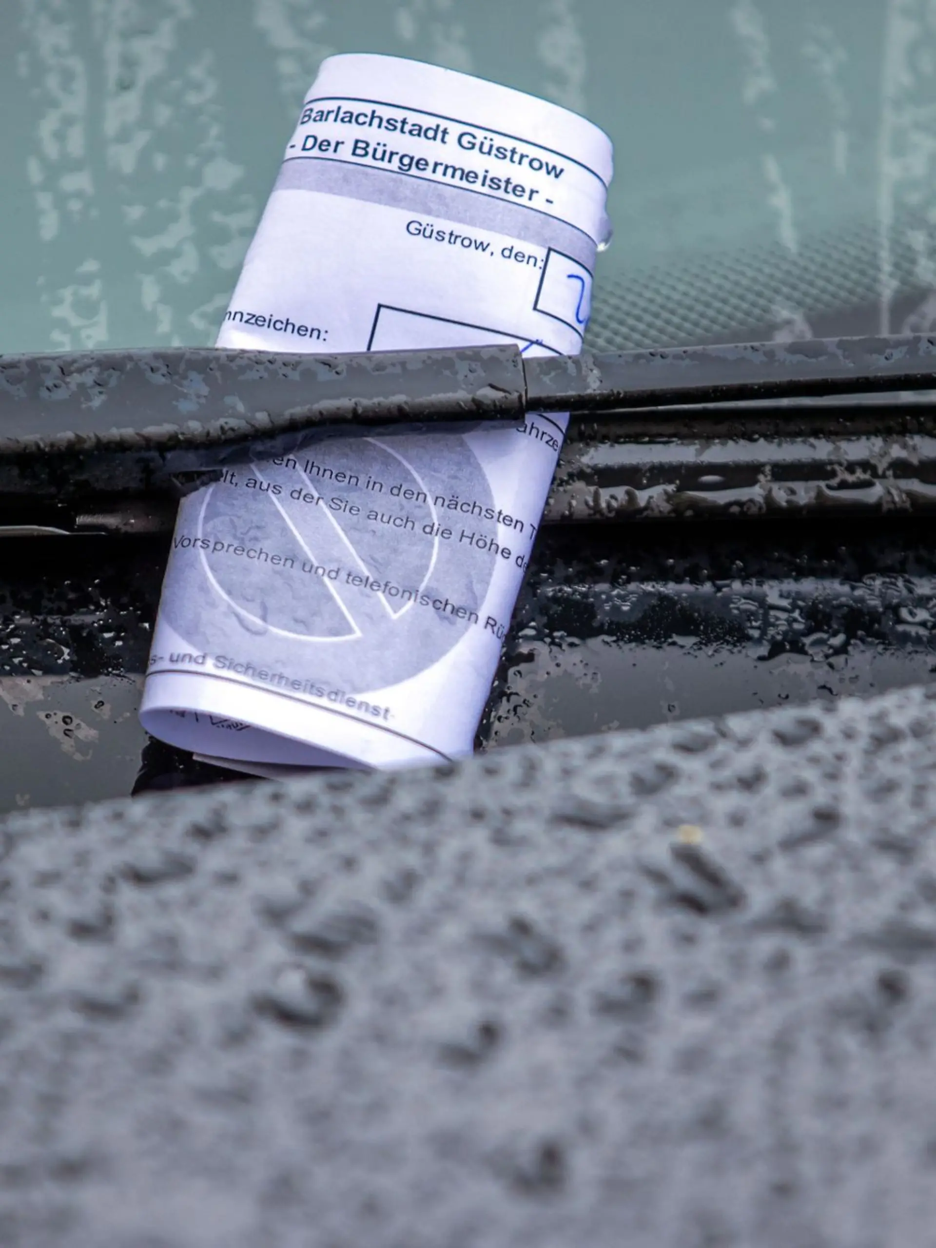 Ein Knöllchen steckt bei Regen unter dem Scheibenwischer eines Autos, das falsch geparkt wurde.