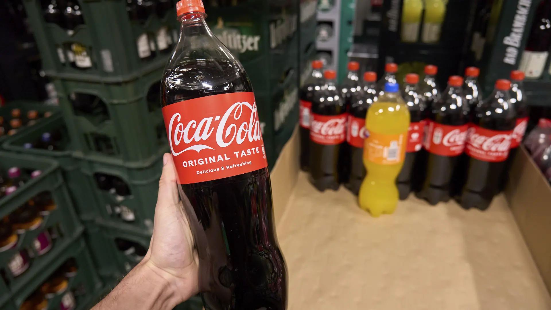 Eine große Coca-Cola-Flasche wird im Supermarkt vor anderen Flaschen und Getränken gezeigt, Softdrink, Getränk kaufen im Getränkemarkt, Flasche, CocaCola, Schraubverschluss, große Flasche, Original Taste, ungesunde Getränke, Softdrinks, Zucker, süß, ungesunde Ernährung, in Hand halten, Ich-Perspektive, Supermarkt, Rewe, Laden, Deutschland