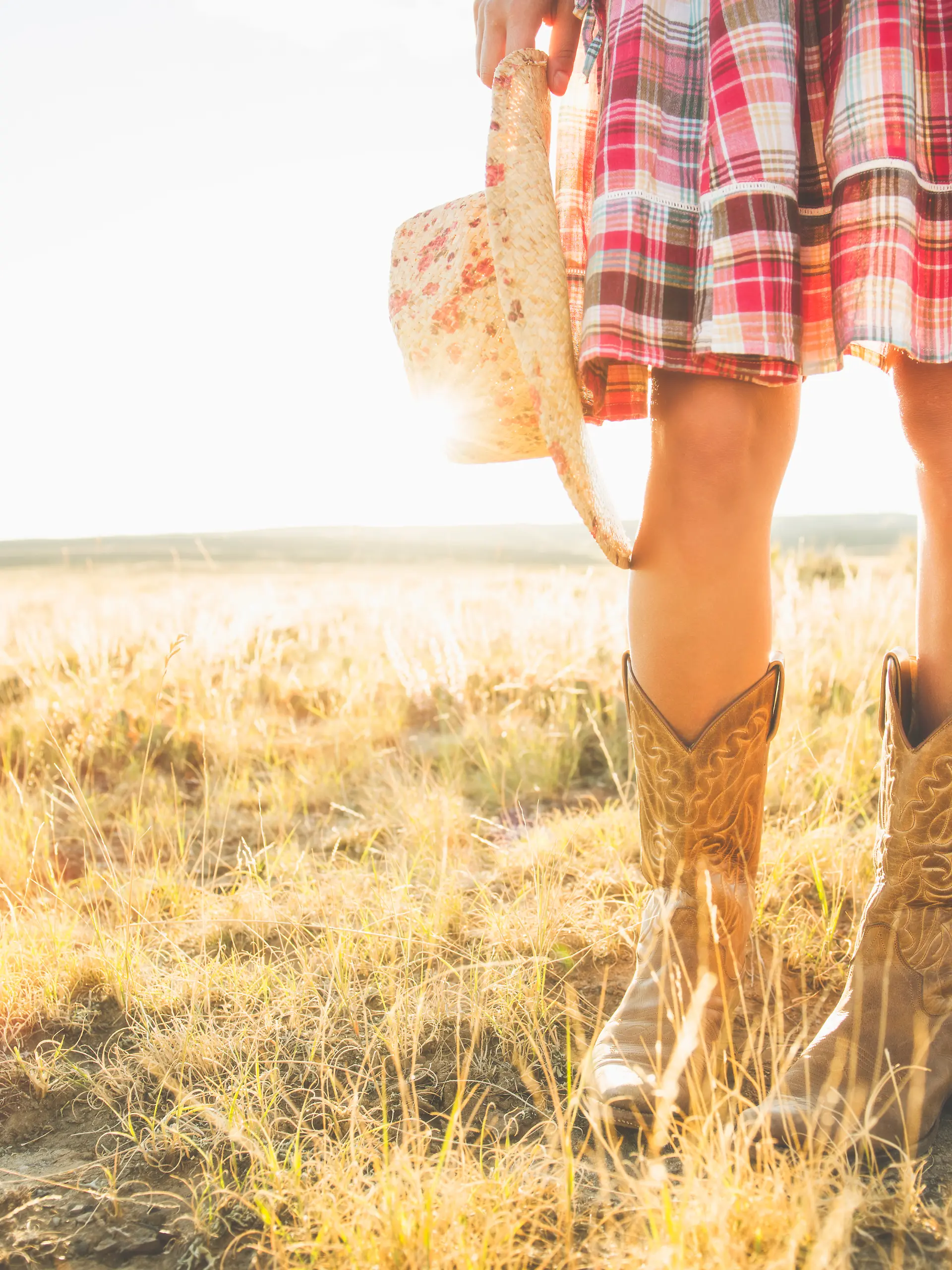 Beine einer hispanischen Frau in Cowboystiefeln, die einen Hut in der Wüste hält – Stockfotografie