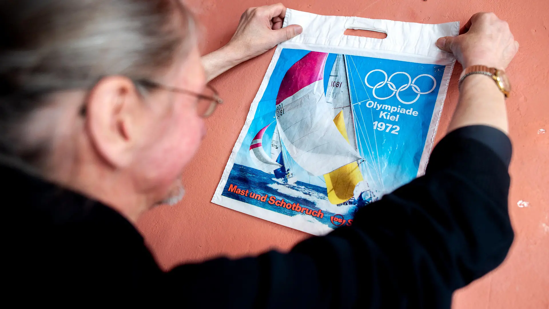 PRODUKTION - 08.05.2023, Bremen: Sammler Jürgen Francke hängt in der Kneipe ·Horner Eck· die erste Plastiktüte seiner Sammlung, die ein Motiv der Olympischen Spiele 1972 zeigt, an eine Wand. Jürgen Francke aus Bremen hat in rund 50 Jahren über 60.000 Plastiktüten gesammelt. In der Kneipe ·Horner Eck· wird eine Auswahl seiner Sammlung gezeigt. Foto: Hauke-Christian Dittrich/dpa +++ dpa-Bildfunk +++