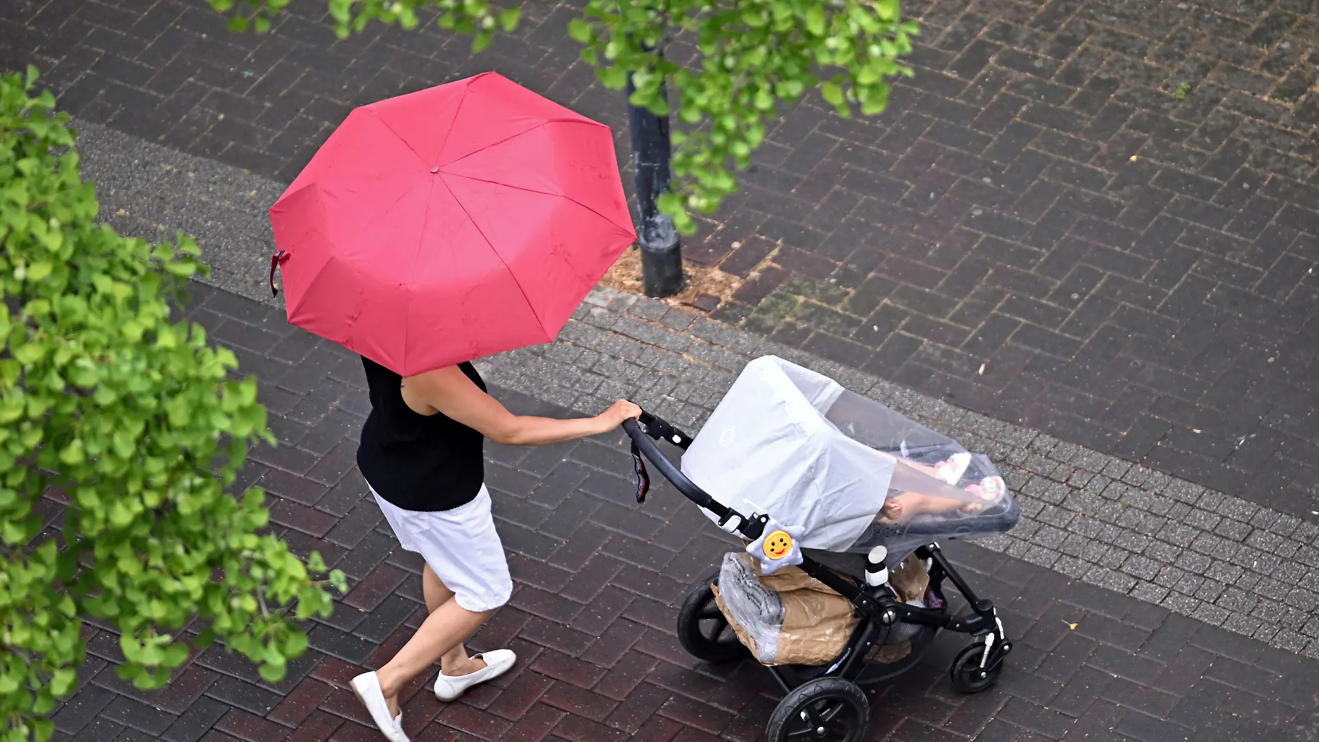 Eine Frau läuft mit einem Kinderwagen und Regenschirm durch Offenbach am Main. Nach Angaben des Deutschen Wetterdienstes besteht bereits am Vormittag in Hessen ein zunehmendes Gewitterrisiko. Im Tagesverlauf sind verbreitet Schauer und Gewitter mit Starkregen, Hagel und Sturmböen möglich.