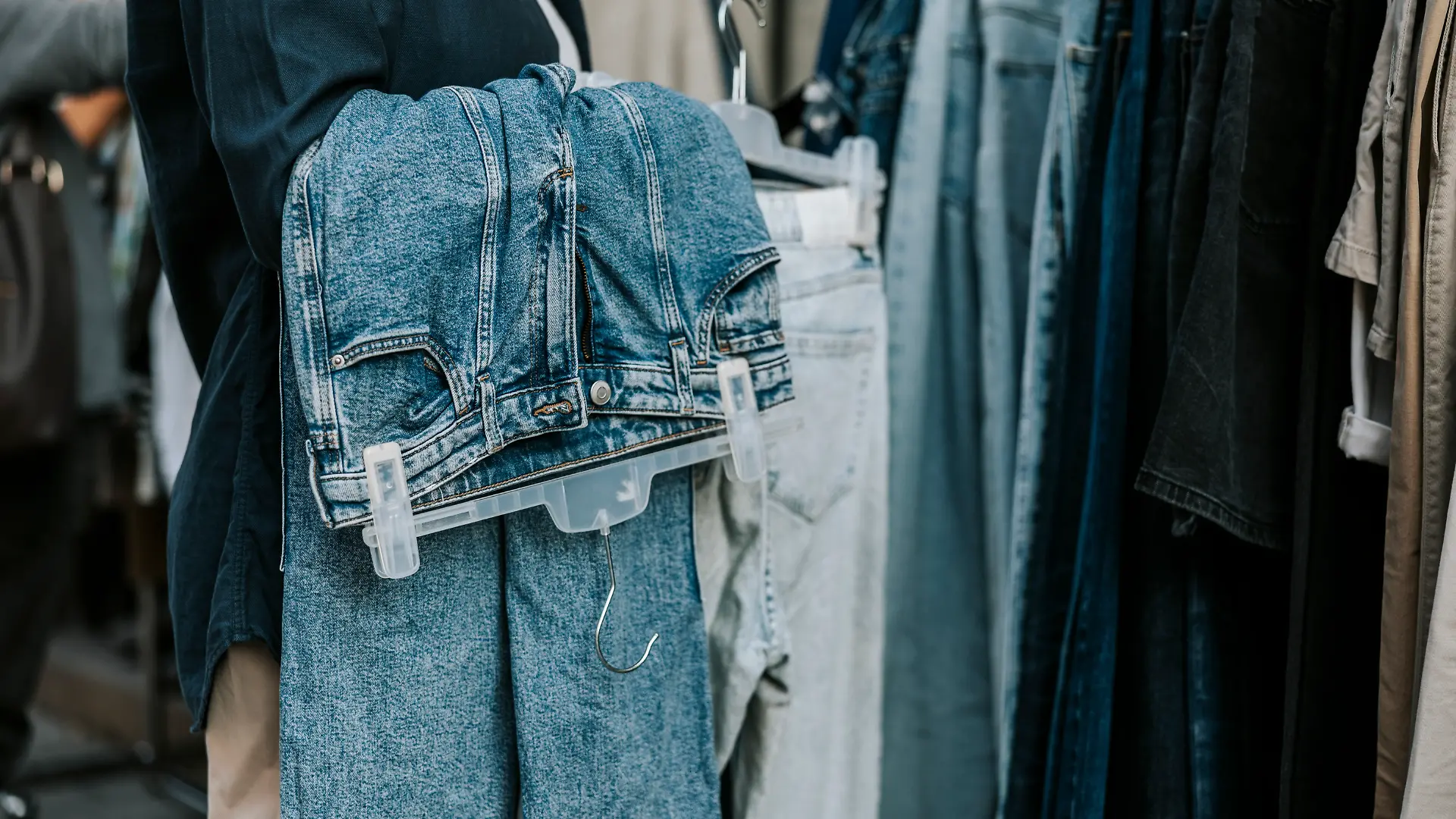 Frau steht im Geschäft mit blauer Jeans, aufgebügelt über dem Arm 