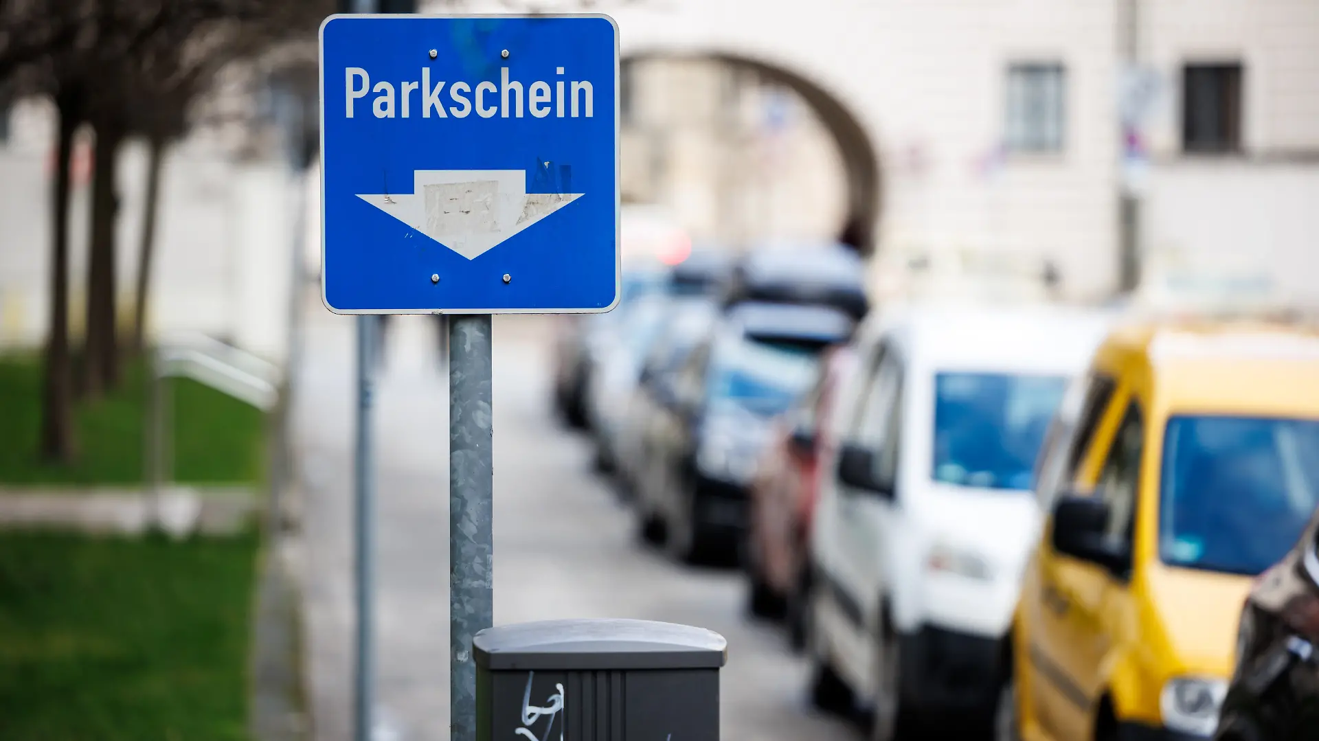Ein Schild weist am Straßenrand neben geparkten Fahrzeugen auf die Position eines Parkscheinautomaten hin.