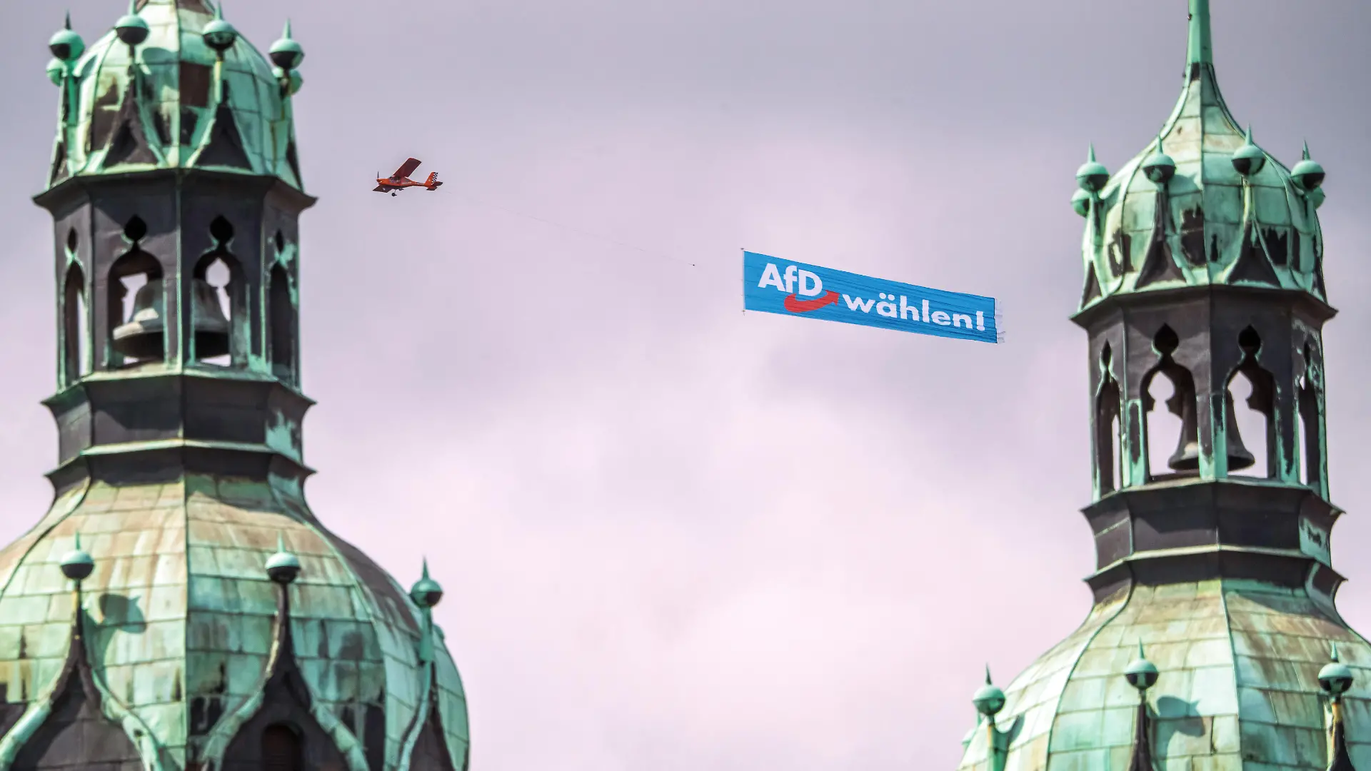 Deutschland, Halle (Saale), 29. August 2026, AfD-Banner über dem Marktplatz, ein Flugzeug mit AfD Wahlwerbung kreist am Samstagmittag über der Altstadt, hier über der Marktkirche, im Bild sind die beiden Hausmannstürme zu sehen, kritische Haltung der evangelischen Kirche zur AfD, an der Marktkirche weiter unten hängt ein Transparent: Mit Menschlichkeit wählen, Landtagswahlen in Sachsen-Anhalt am 6. September, Wahlkampf, Politik,