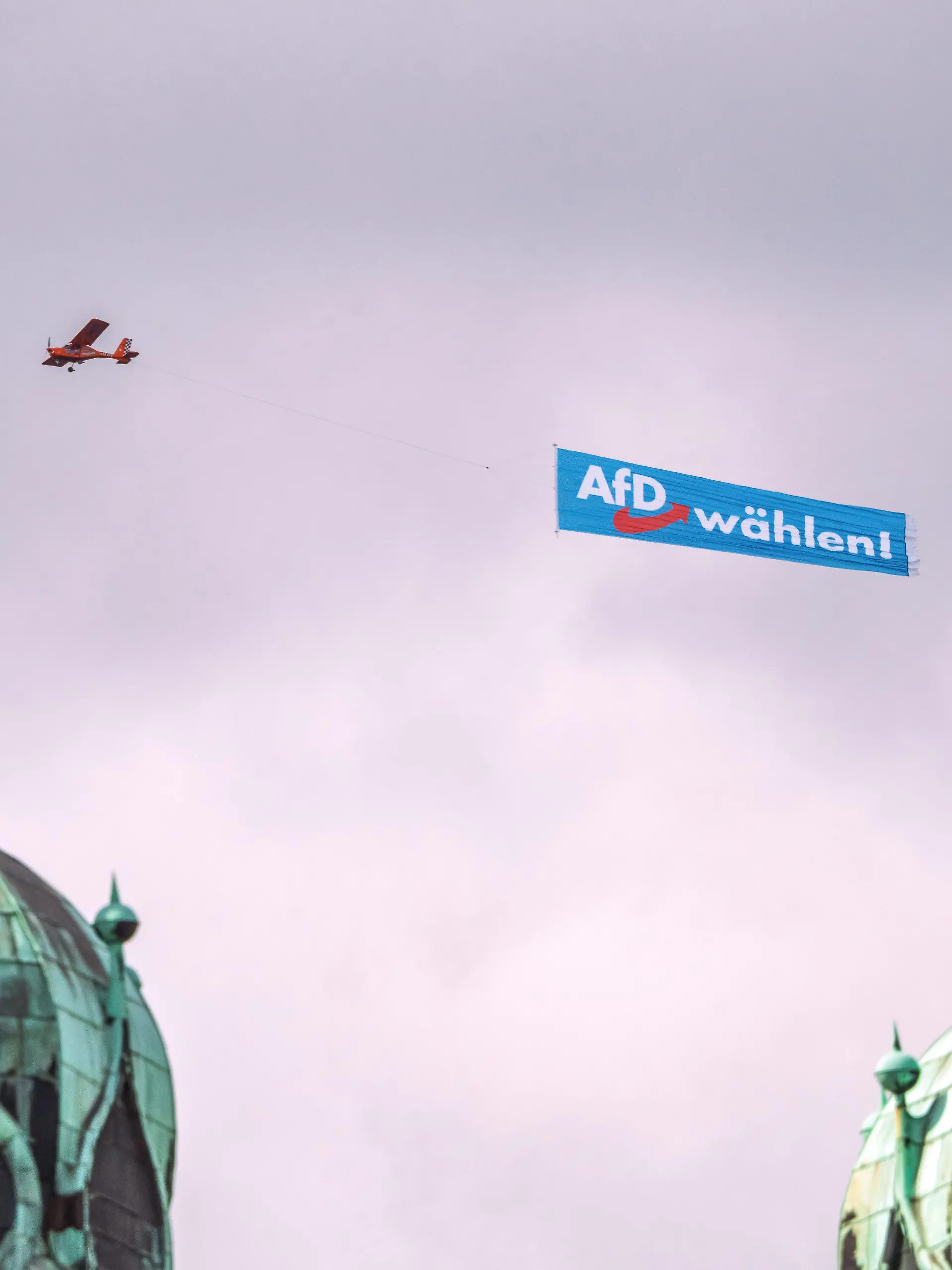 Deutschland, Halle (Saale), 29. August 2026, AfD-Banner über dem Marktplatz, ein Flugzeug mit AfD Wahlwerbung kreist am Samstagmittag über der Altstadt, hier über der Marktkirche, im Bild sind die beiden Hausmannstürme zu sehen, kritische Haltung der evangelischen Kirche zur AfD, an der Marktkirche weiter unten hängt ein Transparent: Mit Menschlichkeit wählen, Landtagswahlen in Sachsen-Anhalt am 6. September, Wahlkampf, Politik,
