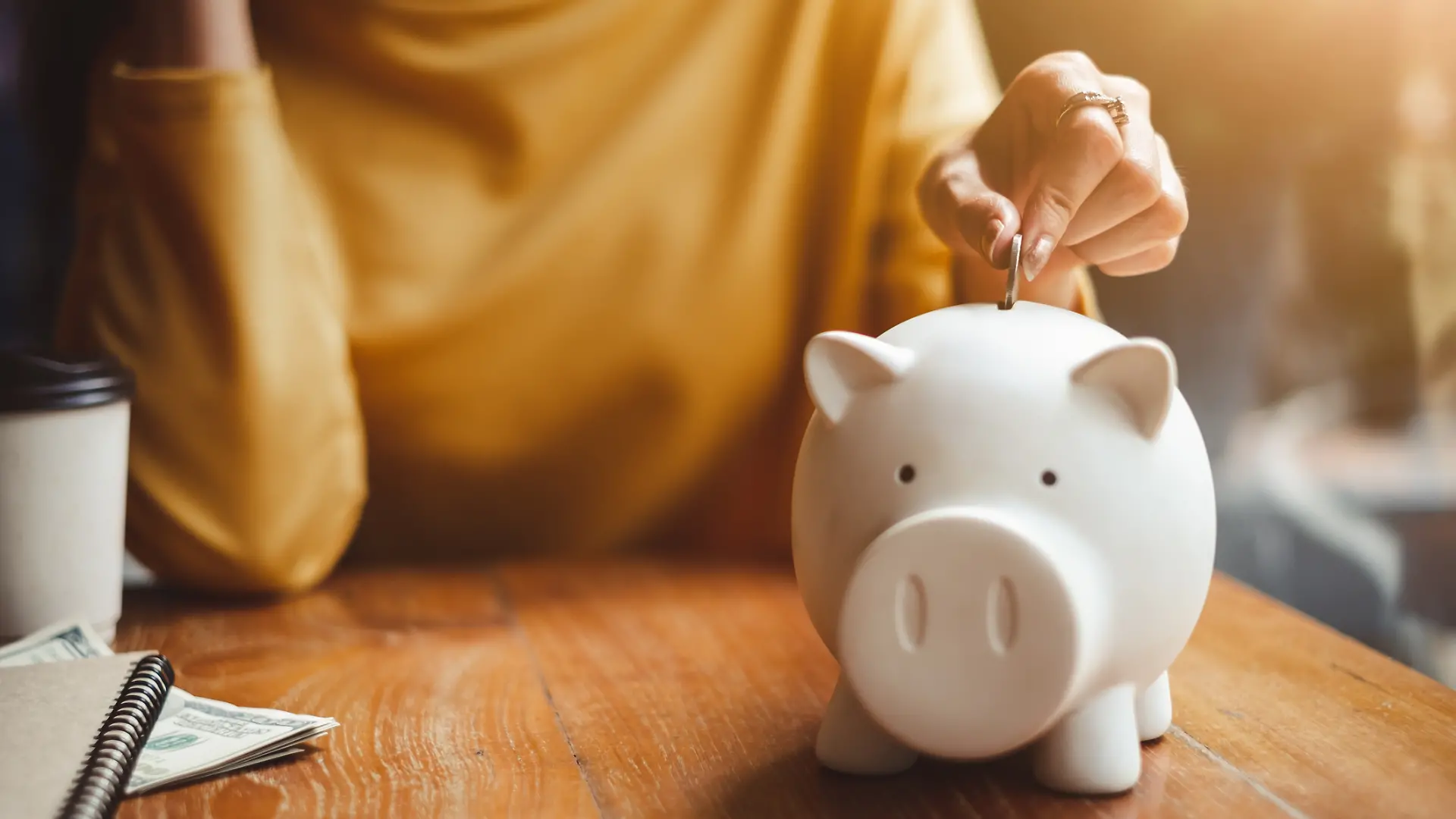 Eine Frau wirft Geld in ihr Sparschwein.