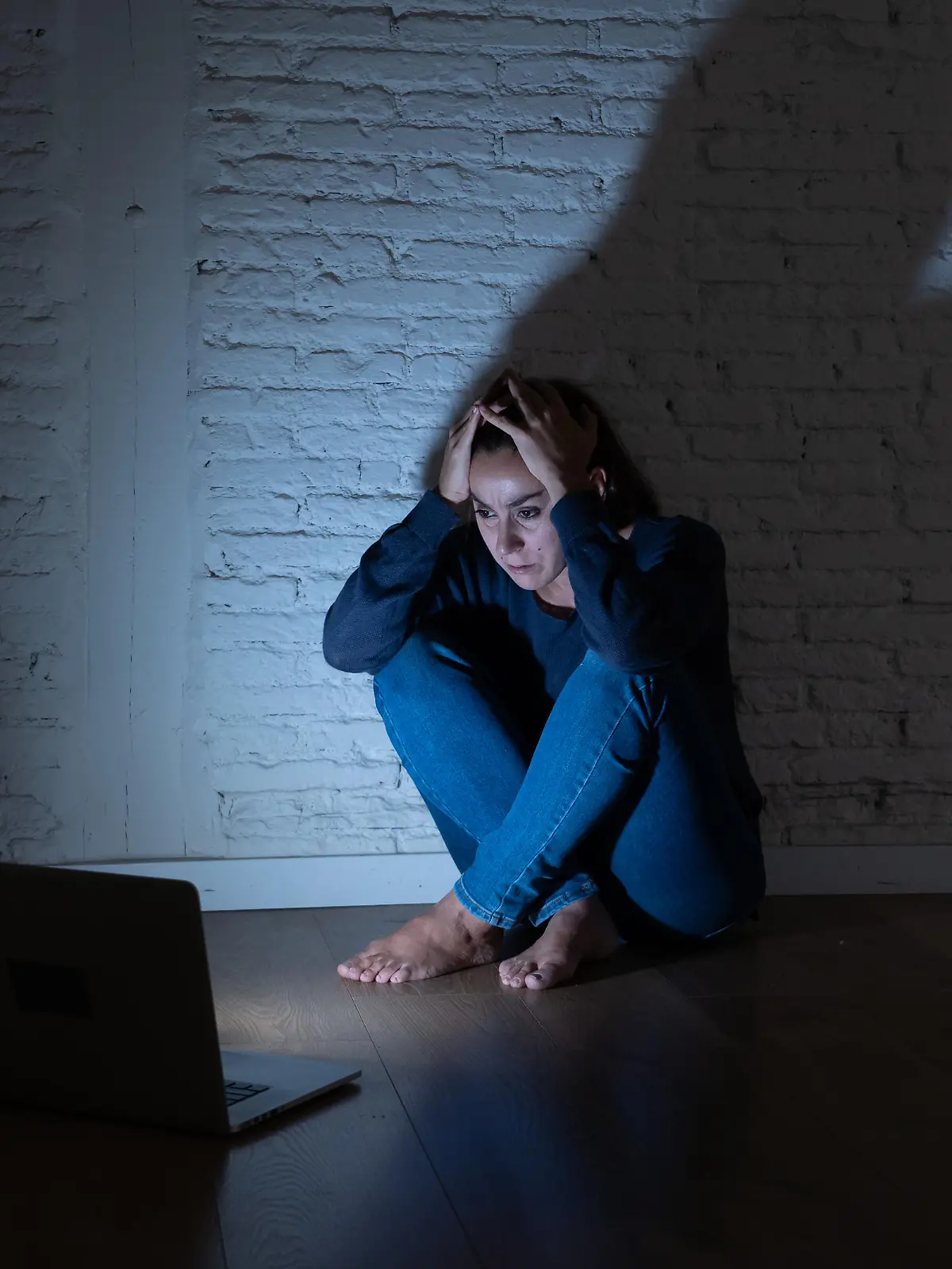 Eine verängstigte Frau sitzt auf dem Boden und schaut auf ihren aufgeklappten Laptop.