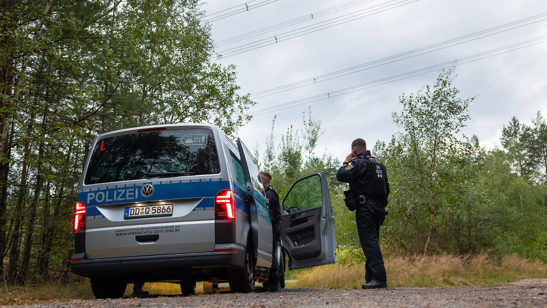 Polizeikräfte stehen in einem Waldstück unter einer Stromtrasse nahe dem Ort Schleife im Landkreis Görlitz. Nach Sabotageversuchen gegen die Stromversorgung in anderen Bundesländern hat die Polizei nun auch in Sachsen «unbekannte Sprengvorrichtungen» entdeckt. +++ dpa-Bildfunk +++