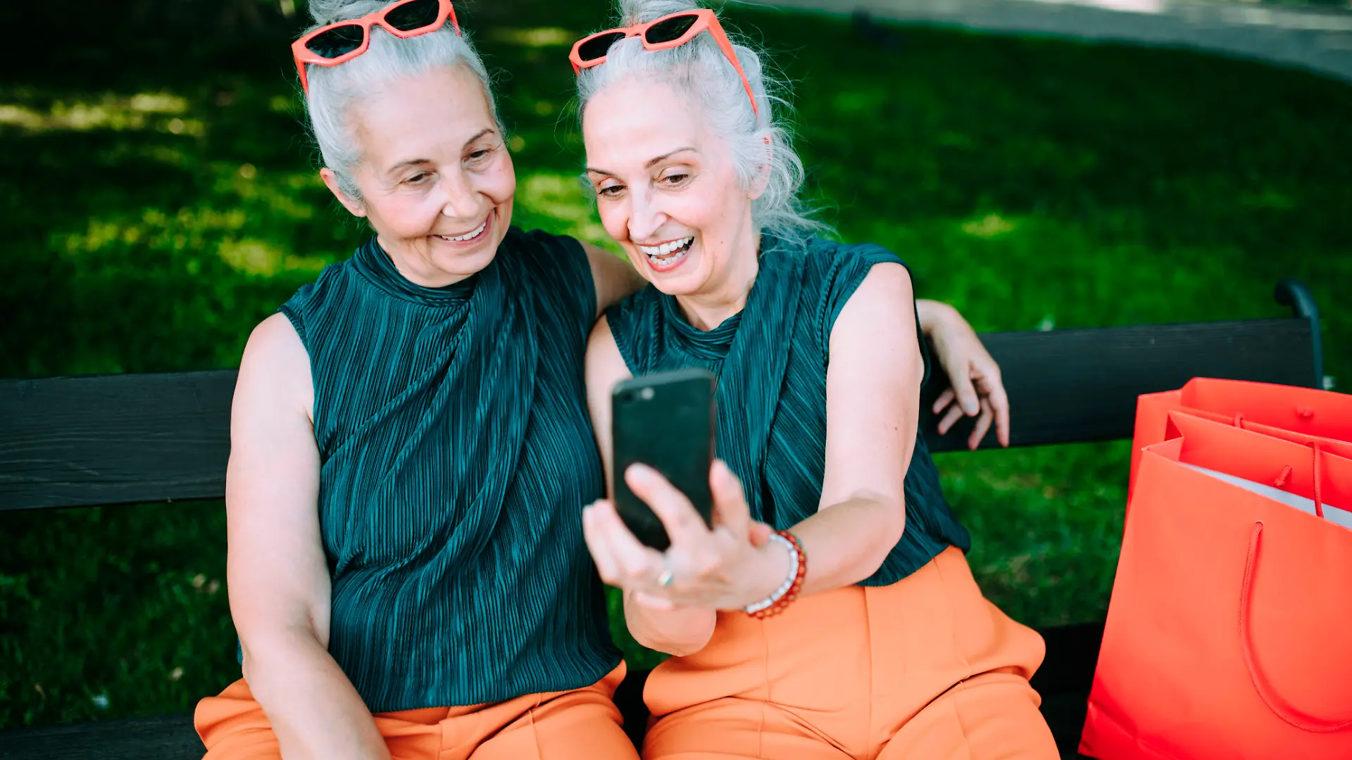 Senior women twins outdoors in city checking smartphone.