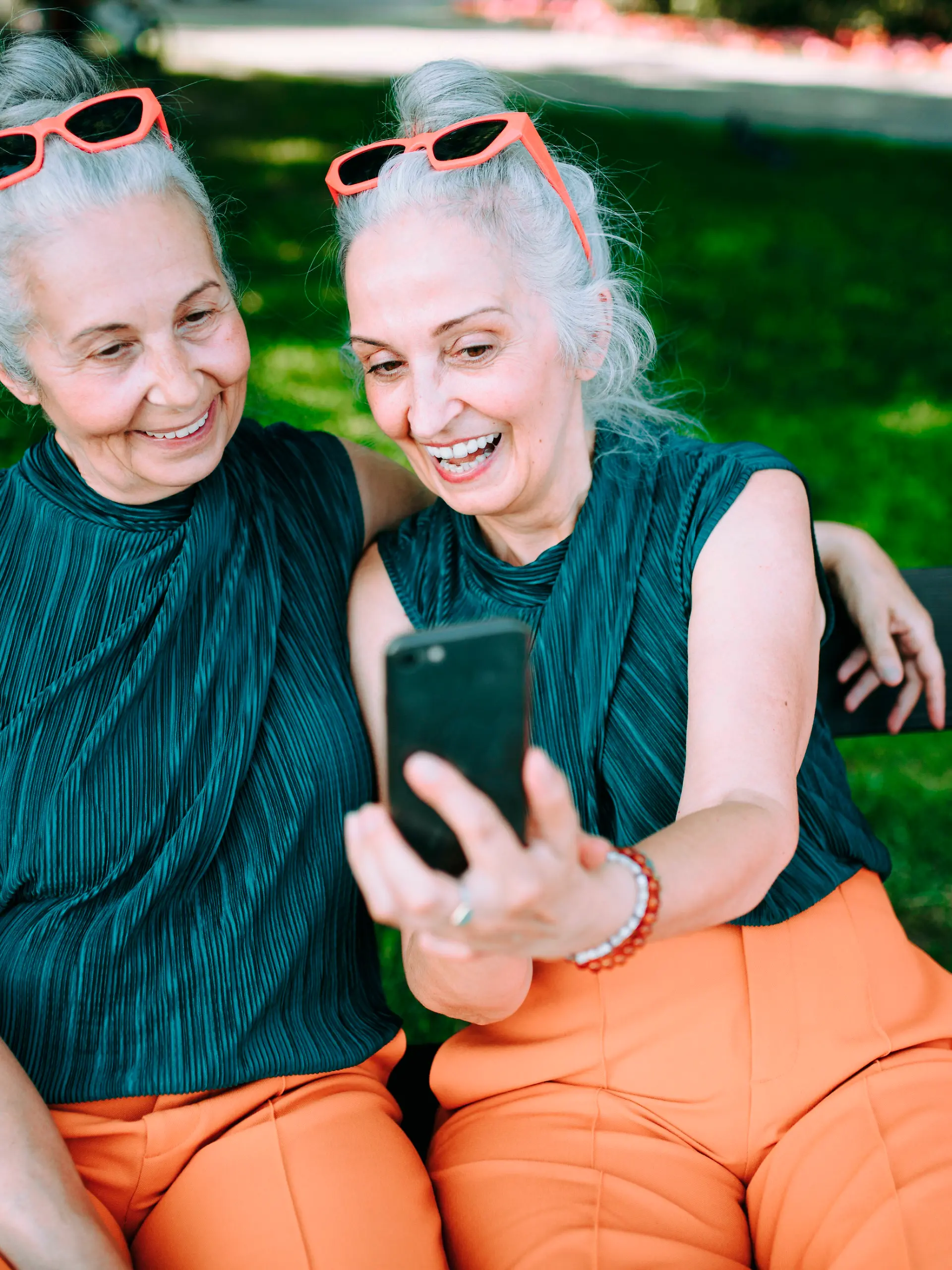 Senior women twins outdoors in city checking smartphone.