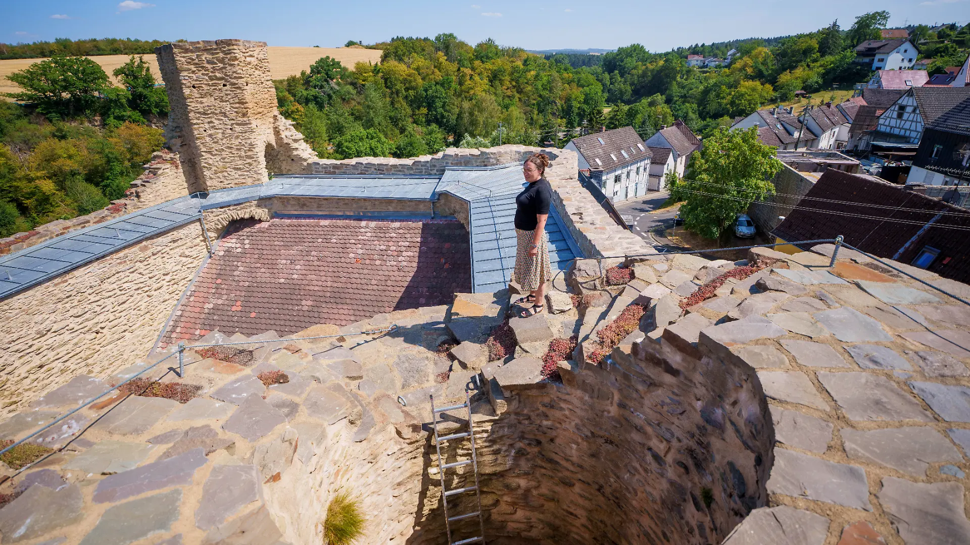 Lauren Liss, Mitbesitzerin der Burg Wallrabenstein, steht ganz oben auf der Mauer der Burgruine. Seit über zehn Jahren ist ein Ehepaar nicht nur Eigentümer eines historischen Fachwerkhauses, sondern auch der mittelalterlichen Burgruine Wallrabenstein, das Wahrzeichen des gleichnamigen Dorfes.