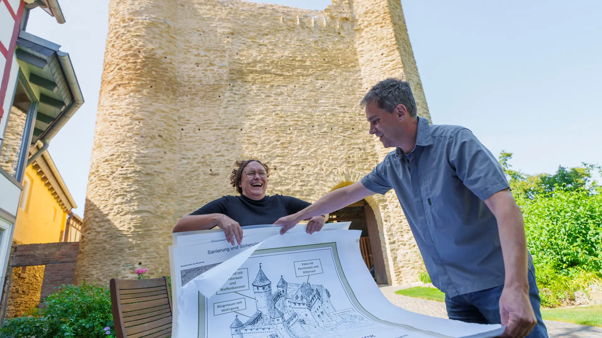 Lauren und Dirk Liss, Besitzer der Burg Wallrabenstein, zeigen anhand einer Rekonstruktionszeichnung von Burgenzeichner Wolfgang Braun, wie die Burganlage um 1450 ausgesehen haben könnte. Seit über zehn Jahren ist das Ehepaar nicht nur Eigentümer eines historischen Fachwerkhauses, sondern auch der mittelalterlichen Burgruine Wallrabenstein, das Wahrzeichen des gleichnamigen Dorfes. (zu dpa "Wie es sich mit eigener Burg im Garten lebt") +++ dpa-Bildfunk +++