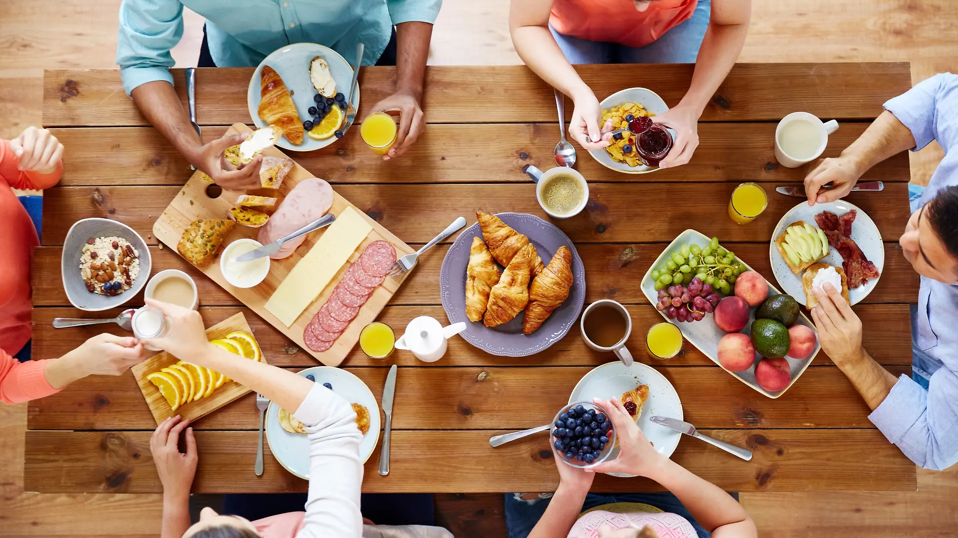 Menschen am Frühstückstisch. Familie, Frühstück, Croissants, Aufschnitt, Brot, Kaffee, Tee.