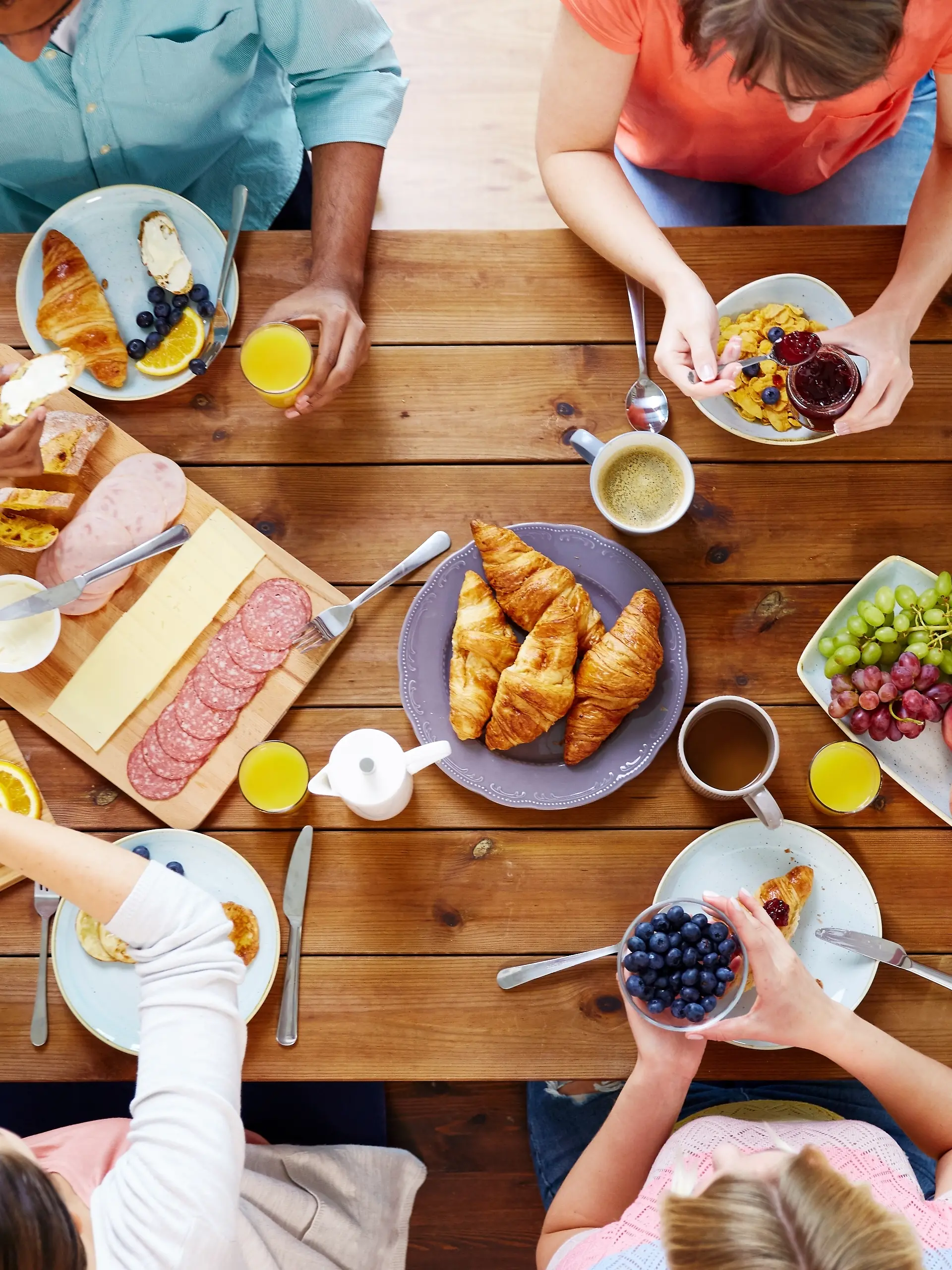 Menschen am Frühstückstisch. Familie, Frühstück, Croissants, Aufschnitt, Brot, Kaffee, Tee.