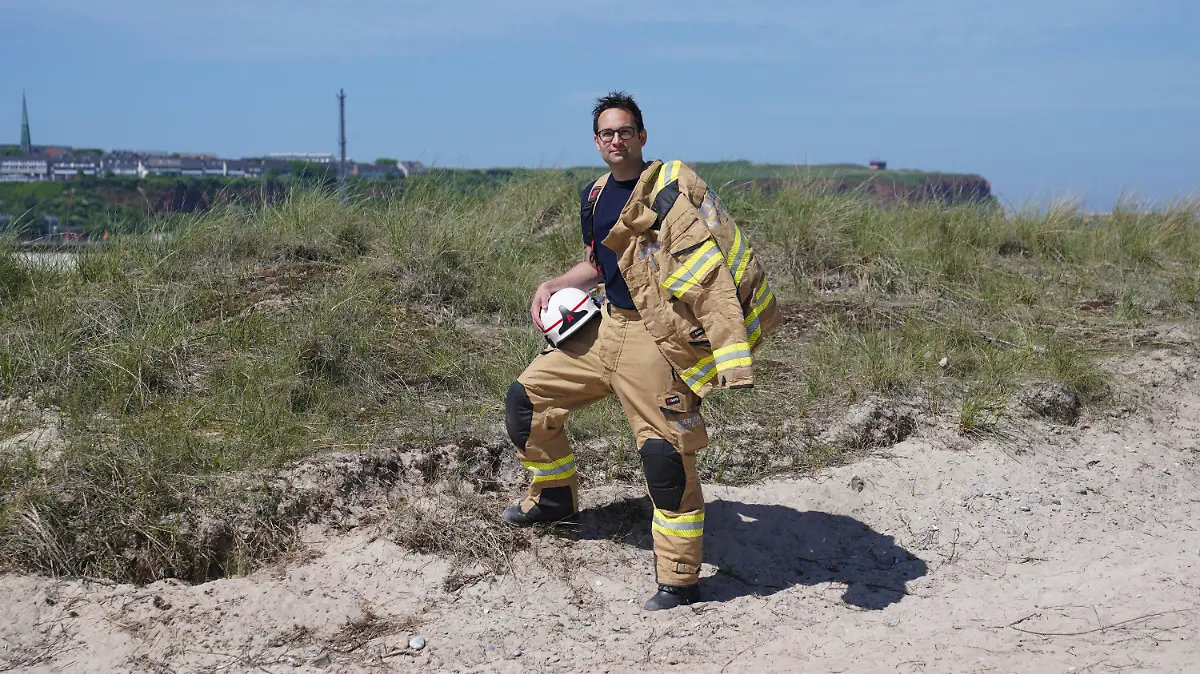 16.06.2021, Schleswig-Holstein, Helgoland: Felix Vorndran von der Freiwilligen Feuerwehr Bergisch-Gladbach steht an der Feuerwehrwache während seines Dünendienstes auf der Düne der Hochseeinsel Helgoland. Angenehmes mit dem Nützlichen verbinden können Feuerwehrleute aus ganz Deutschland in der Saison auf der Hochseeinsel Helgoland. Die Gemeinde sucht für die Sicherstellung des Brandschutzes auf der Düne freiwillige Feuerwehrkameradinnen und -kameraden, die mit Ihrem Einsatz die touristische Nutzung der Düne aufrechterhalten. Untergebracht werden die Feuerwehrleute vom Festland in Bungalows auf der Düne, bis zu drei Familienangehörige dürfen kostenlos mitreisen. (zu dpa ·Feuerwehrleute helfen in ihrem Urlaub beim Brandschutz auf Helgoland·) Foto: Marcus Brandt/dpa +++ dpa-Bildfunk +++