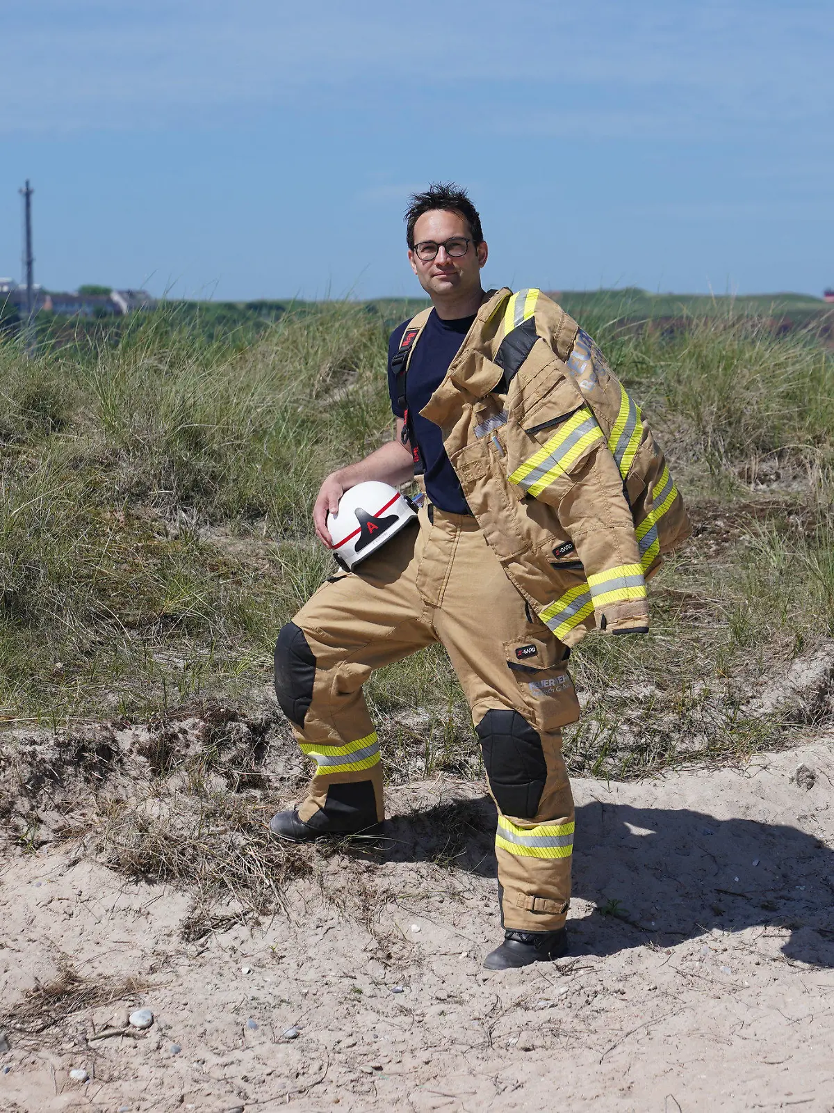 16.06.2021, Schleswig-Holstein, Helgoland: Felix Vorndran von der Freiwilligen Feuerwehr Bergisch-Gladbach steht an der Feuerwehrwache während seines Dünendienstes auf der Düne der Hochseeinsel Helgoland. Angenehmes mit dem Nützlichen verbinden können Feuerwehrleute aus ganz Deutschland in der Saison auf der Hochseeinsel Helgoland. Die Gemeinde sucht für die Sicherstellung des Brandschutzes auf der Düne freiwillige Feuerwehrkameradinnen und -kameraden, die mit Ihrem Einsatz die touristische Nutzung der Düne aufrechterhalten. Untergebracht werden die Feuerwehrleute vom Festland in Bungalows auf der Düne, bis zu drei Familienangehörige dürfen kostenlos mitreisen. (zu dpa ·Feuerwehrleute helfen in ihrem Urlaub beim Brandschutz auf Helgoland·) Foto: Marcus Brandt/dpa +++ dpa-Bildfunk +++