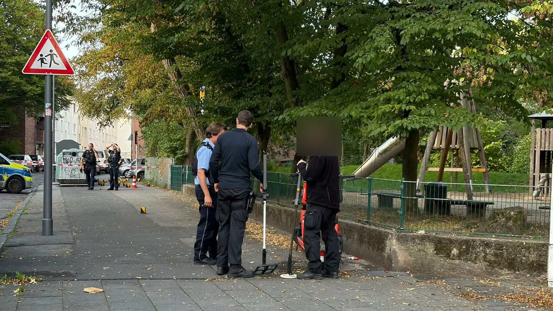 Polizisten in Köln-Mülheim suchen nach Schüssen auf ein Wohn- und Geschäftshaus die Gegend nach Patronenhülsen ab.